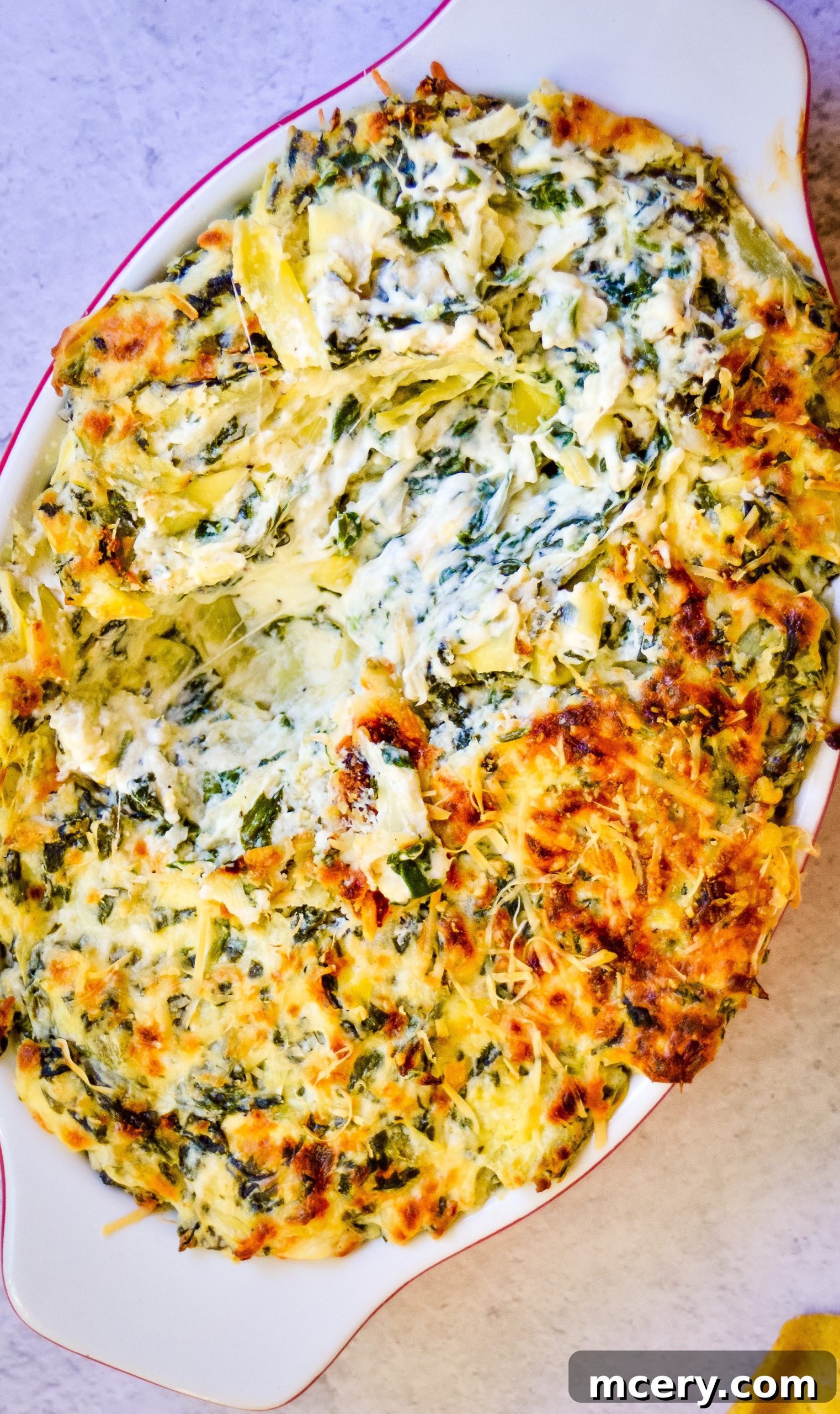 Decadent Spinach Artichoke Dip 3 A top-down view of a large baking dish filled with freshly baked spinach artichoke dip, garnished with fresh herbs, ready to be served at a party.
