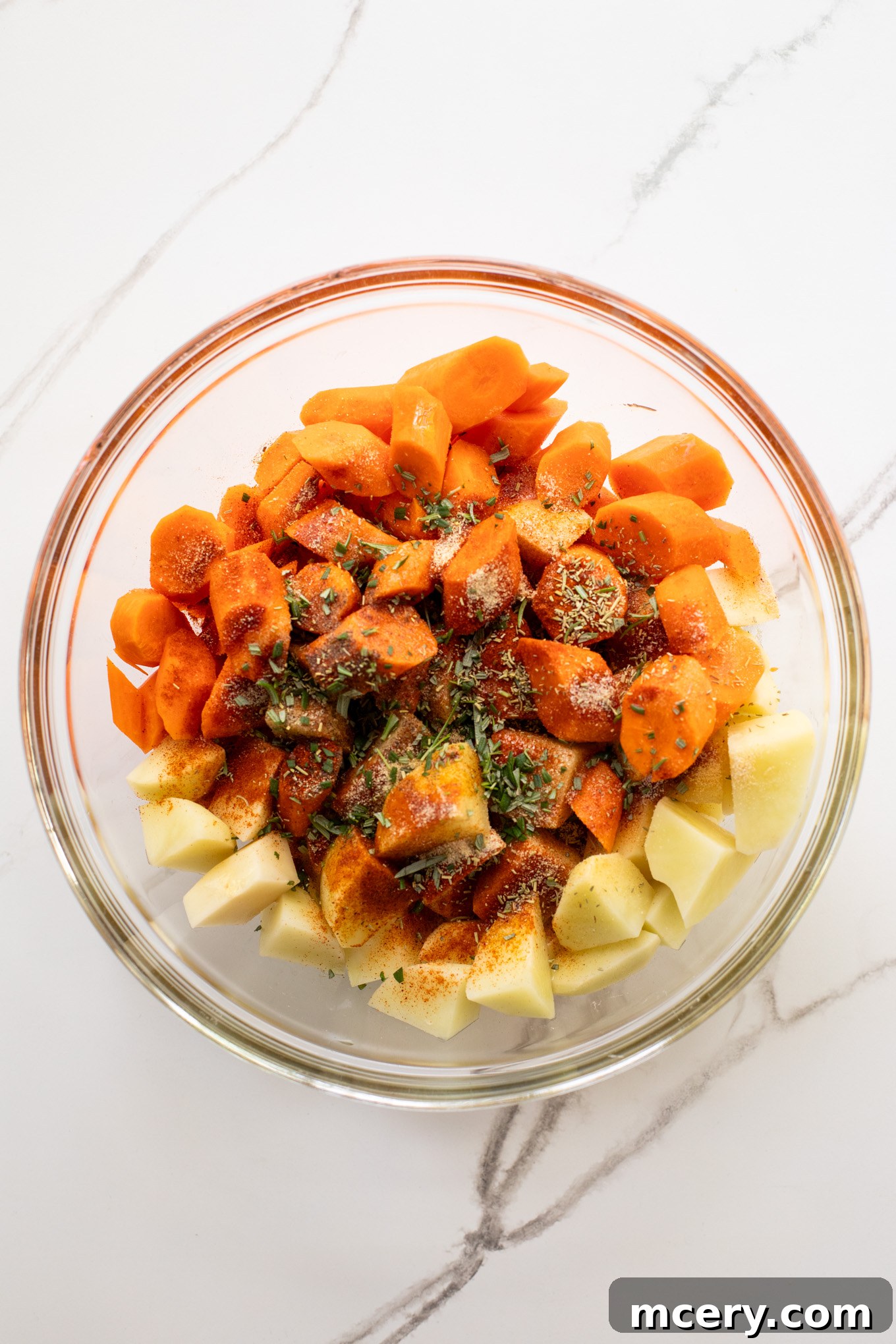 Caramelized Carrots and Crispy Potatoes 4 cut up carrots and potatoes in a glass bowl with oil and spices.