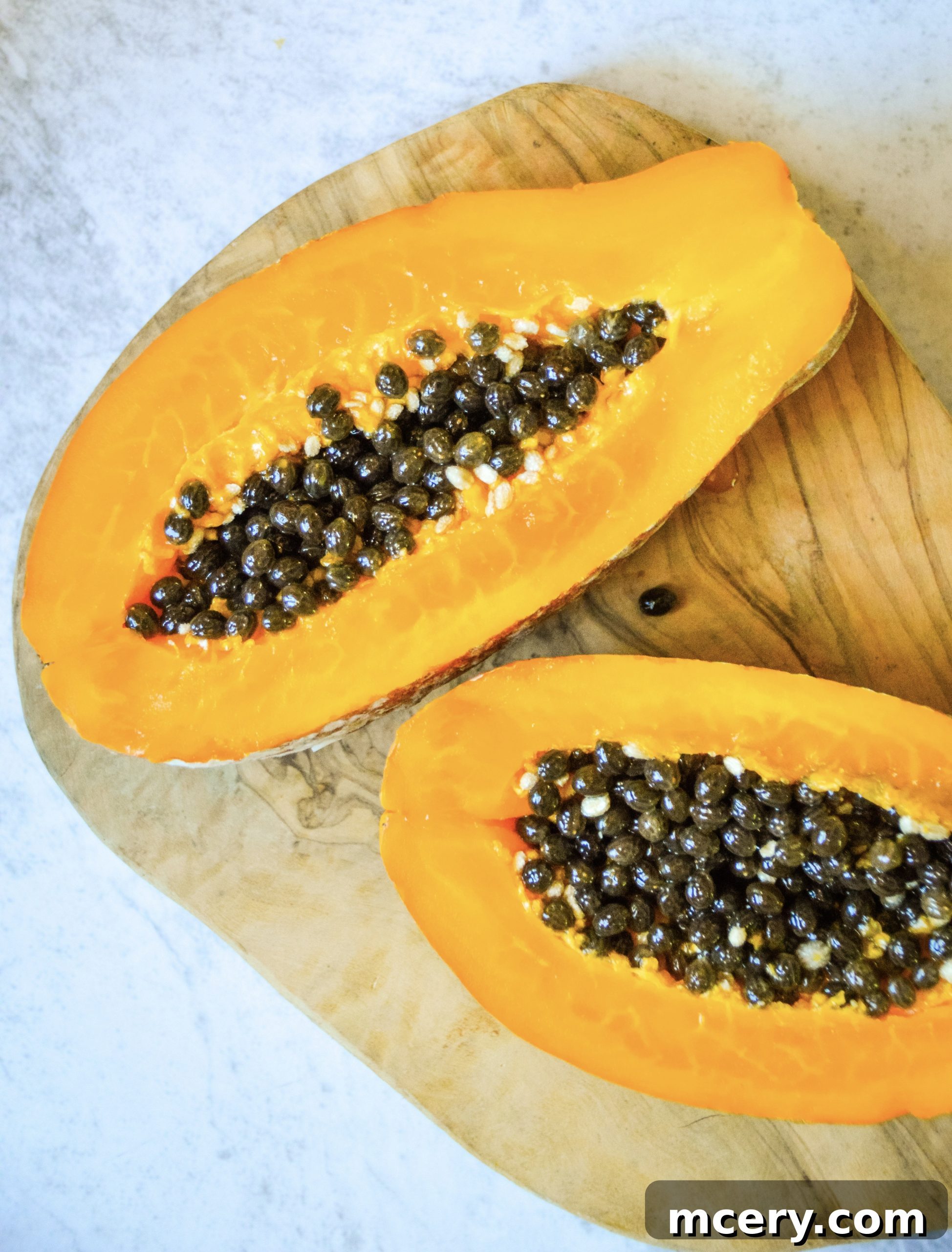 Two glasses of Papaya Dream Smoothie, one in the foreground with a spoon, showing its creamy texture, on a rustic wooden surface.
