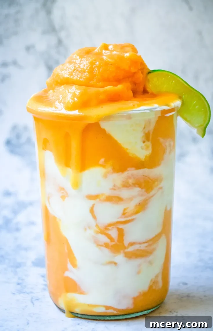 Tropical Papaya Fantasy 5 A layered Papaya Dream Smoothie in a glass, featuring swirls of orange and white, topped with a dollop of papaya purée. A wedge of lime is placed on the rim. The background is a soft, blurry gray.
