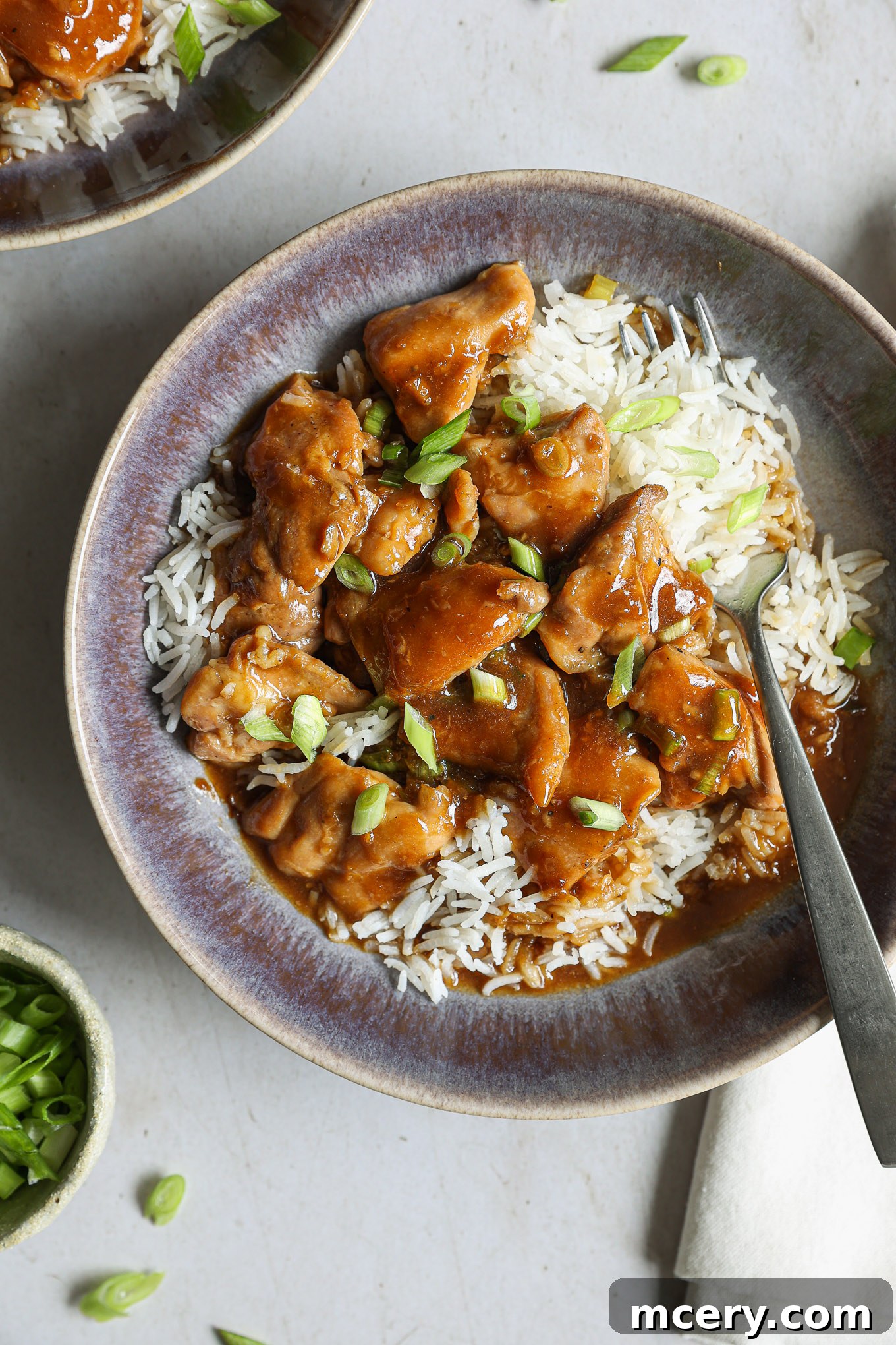 Whip Up Delicious Homemade Chicken Teriyaki 10 A bowl of cooked teriyaki chicken, garnished with scallions and sesame seeds, served over fluffy white rice.