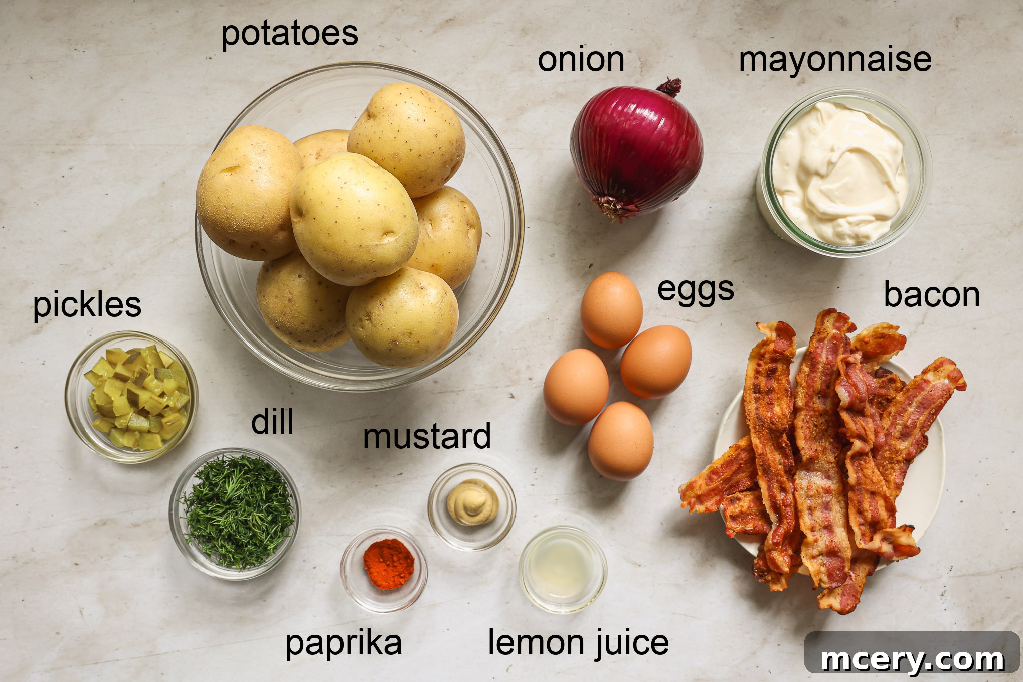Various fresh ingredients laid out on a wooden board, including Yukon Gold potatoes, red onion, fresh dill, hard-boiled eggs, and a bowl of mayonnaise.