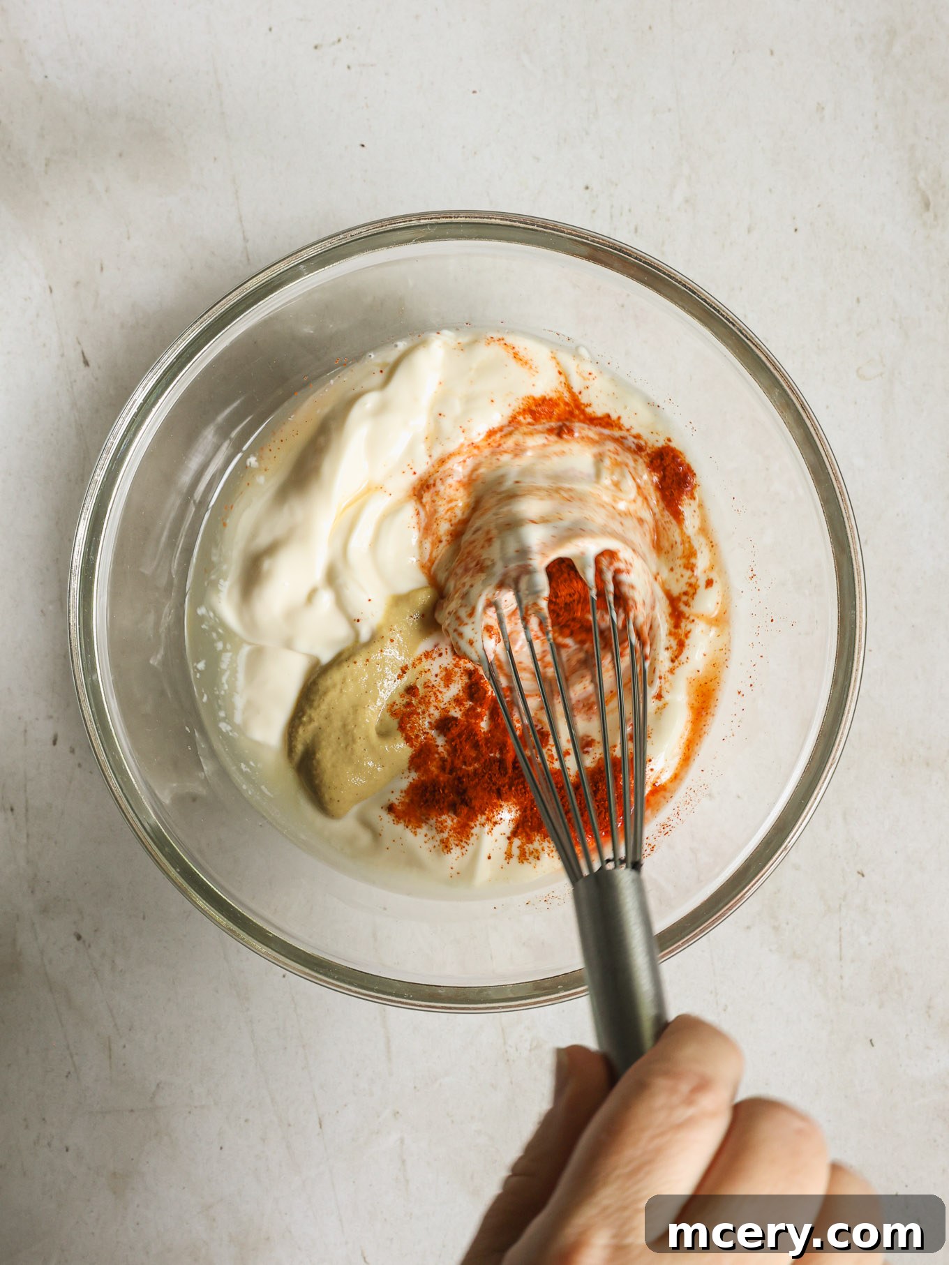 A creamy dressing in a small bowl being whisked with a metal whisk.
