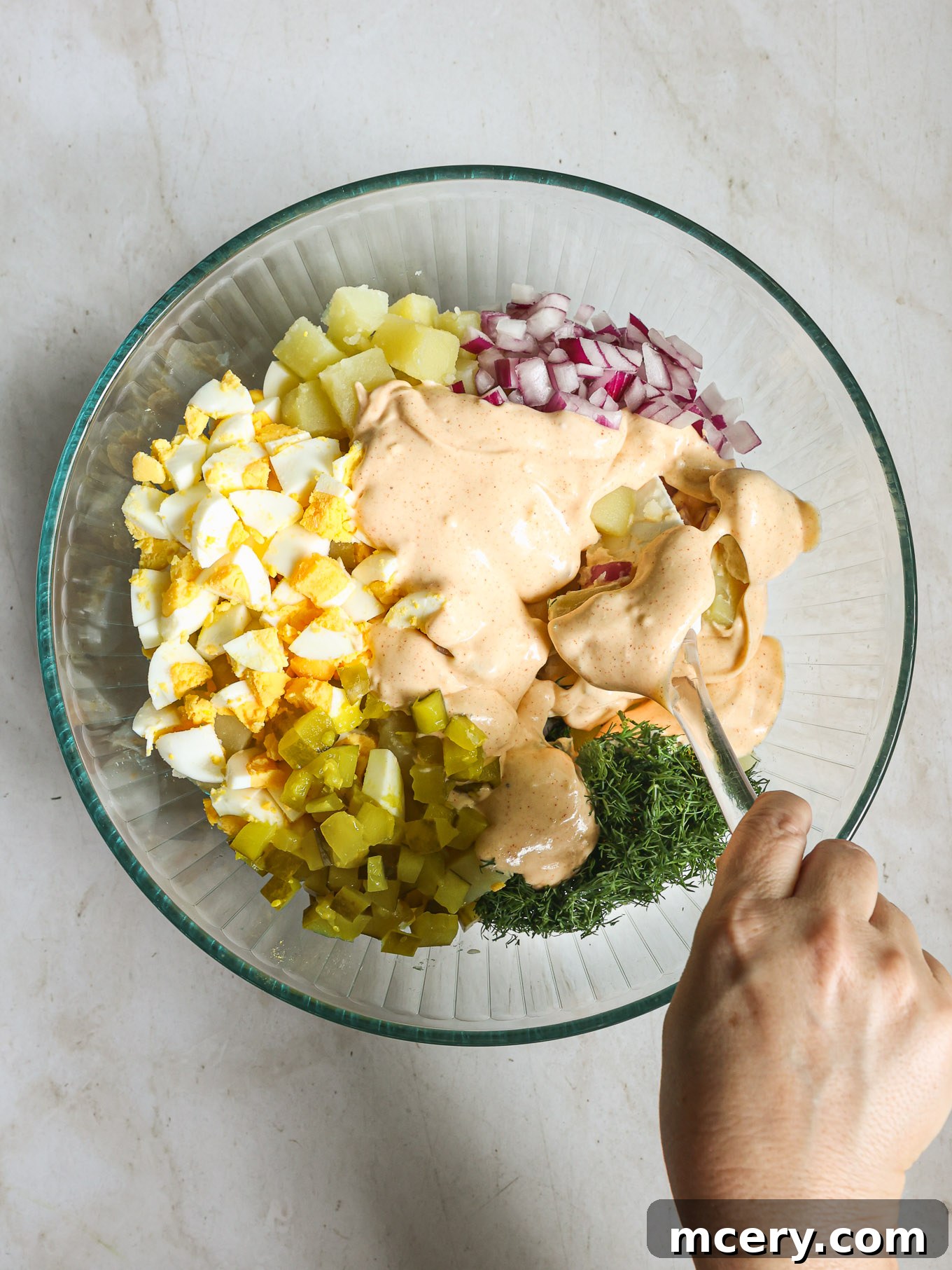 Chopped potatoes, red onions, pickles, and hard-boiled eggs in a large glass mixing bowl.