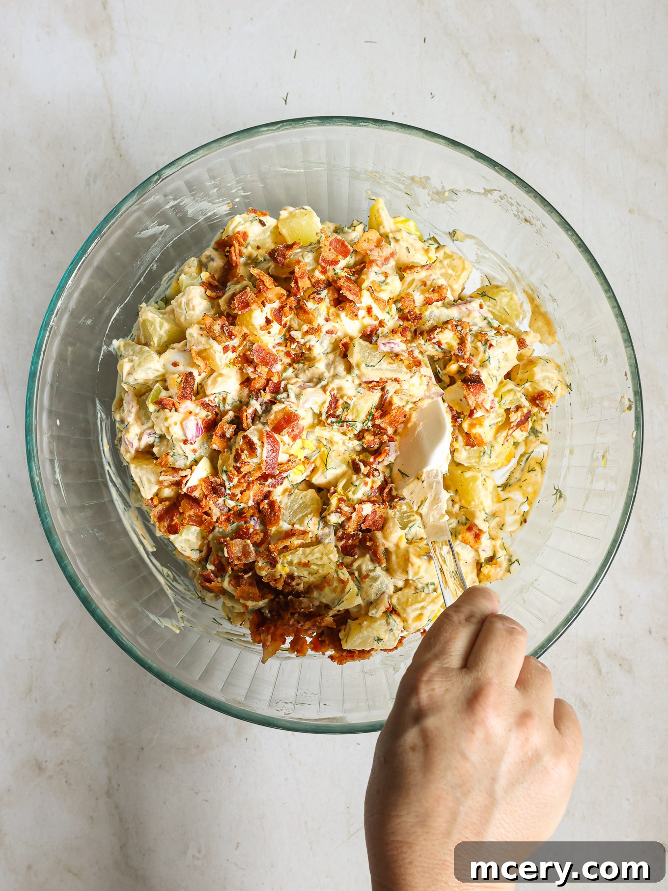 Creamy potato salad topped with crumbled crispy bacon in a white serving bowl.