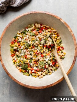 A bowl of fresh white bean salad with a wooden spoon, showcasing vibrant vegetables and creamy beans.
