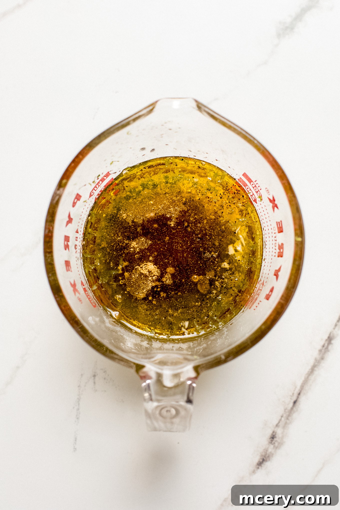 Ingredients for the dressing in a glass measuring cup, including olive oil, lime, garlic, cumin, and honey.