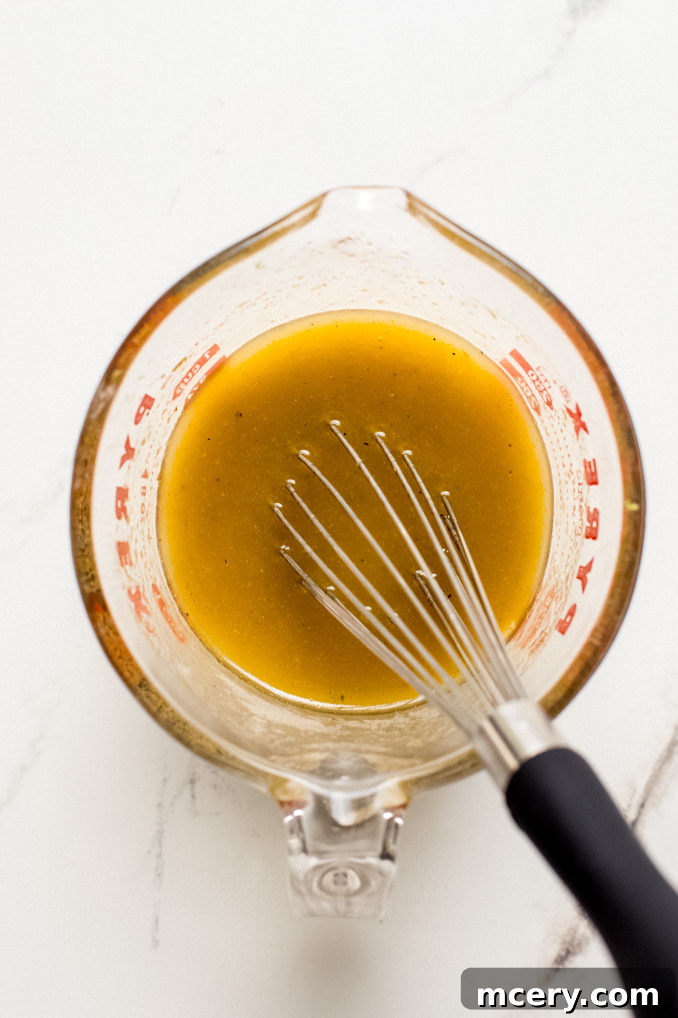 The dressing ingredients have been thoroughly whisked together in a glass measuring cup, showing a smooth, emulsified mixture.