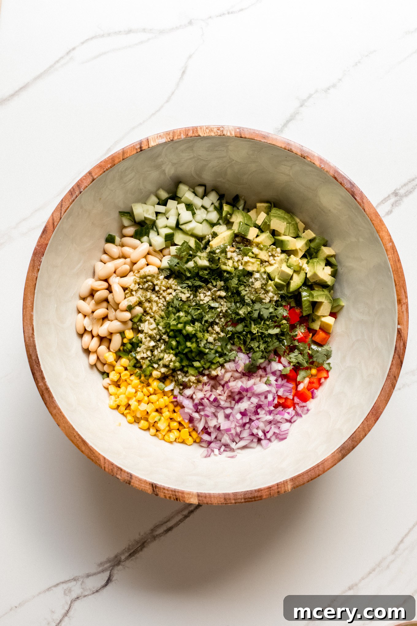 Chopped vegetables and rinsed white beans are gathered in a large mixing bowl, ready for the dressing.