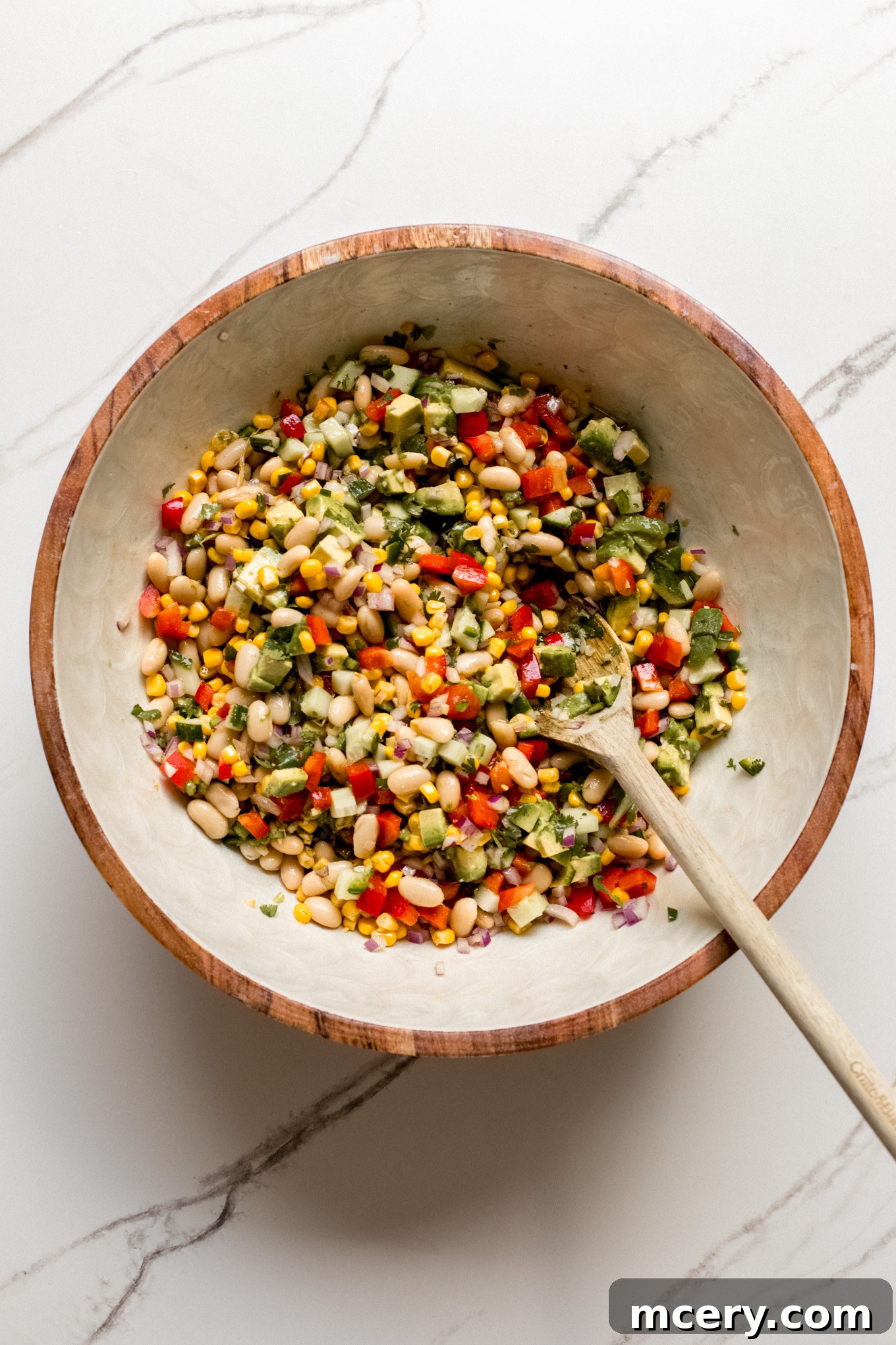 The dressing has been poured over the salad ingredients, and a spoon is shown tossing the mixture gently.