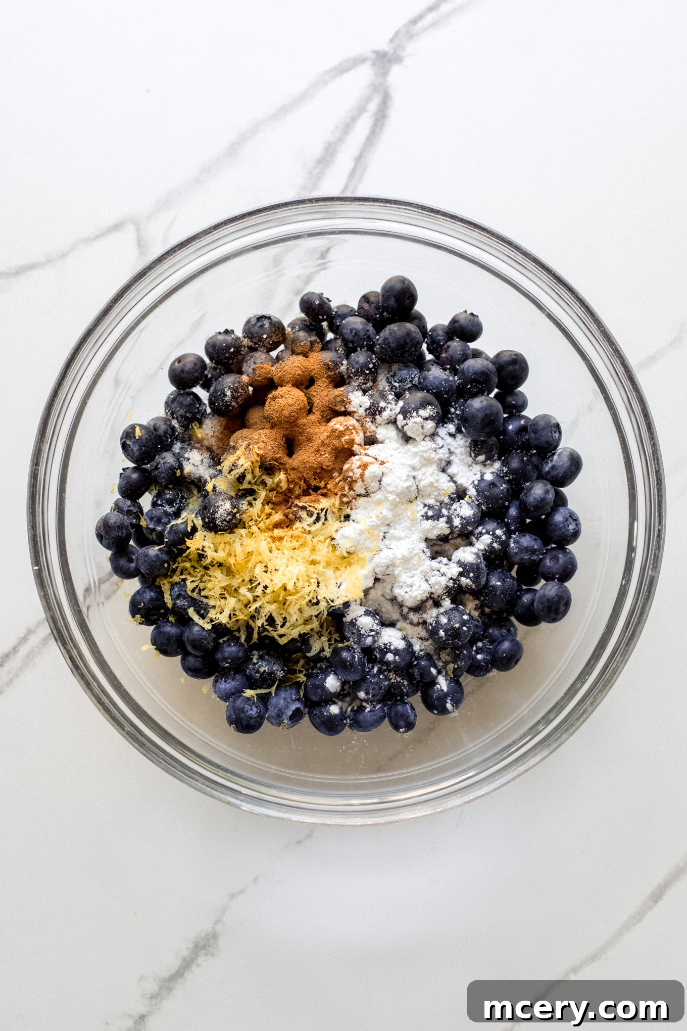 Golden Oat Topped Blueberry Crisp 4 Blueberries with lemon zest and cinnamon being mixed in a glass bowl.
