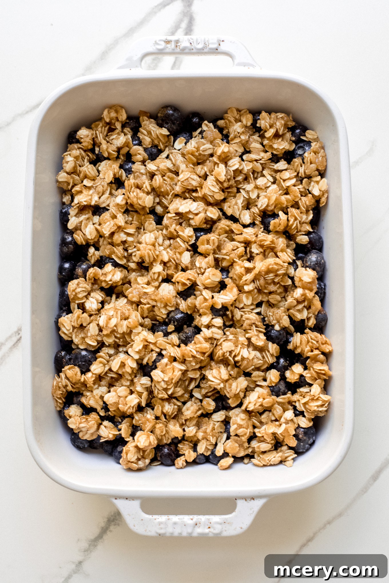 Golden Oat Topped Blueberry Crisp 9 Blueberries topped with oat and flour crumble topping in a baking dish, ready for the oven.