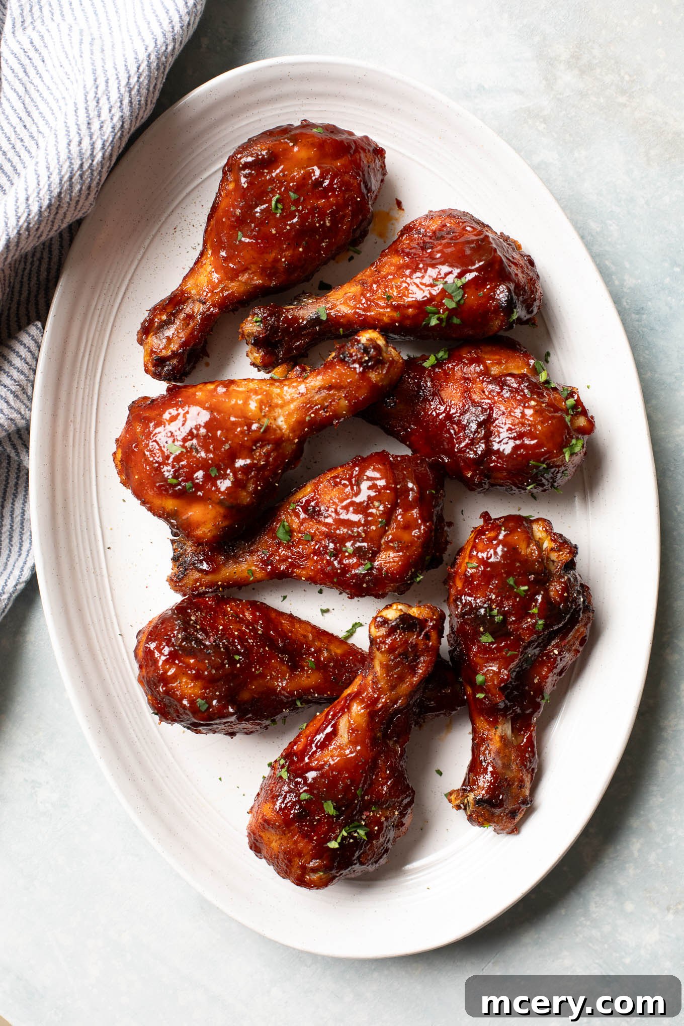 Sweet & Smoky Oven-Baked BBQ Drumsticks 2 Roasted chicken legs on an oval platter topped with BBQ sauce, ready to serve.
