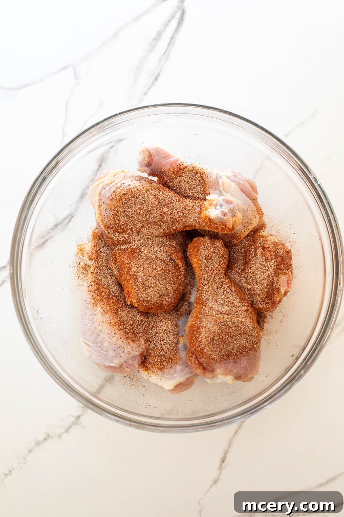 Sweet & Smoky Oven-Baked BBQ Drumsticks 6 Chicken legs in a glass bowl, thoroughly coated with a dry spice rub.