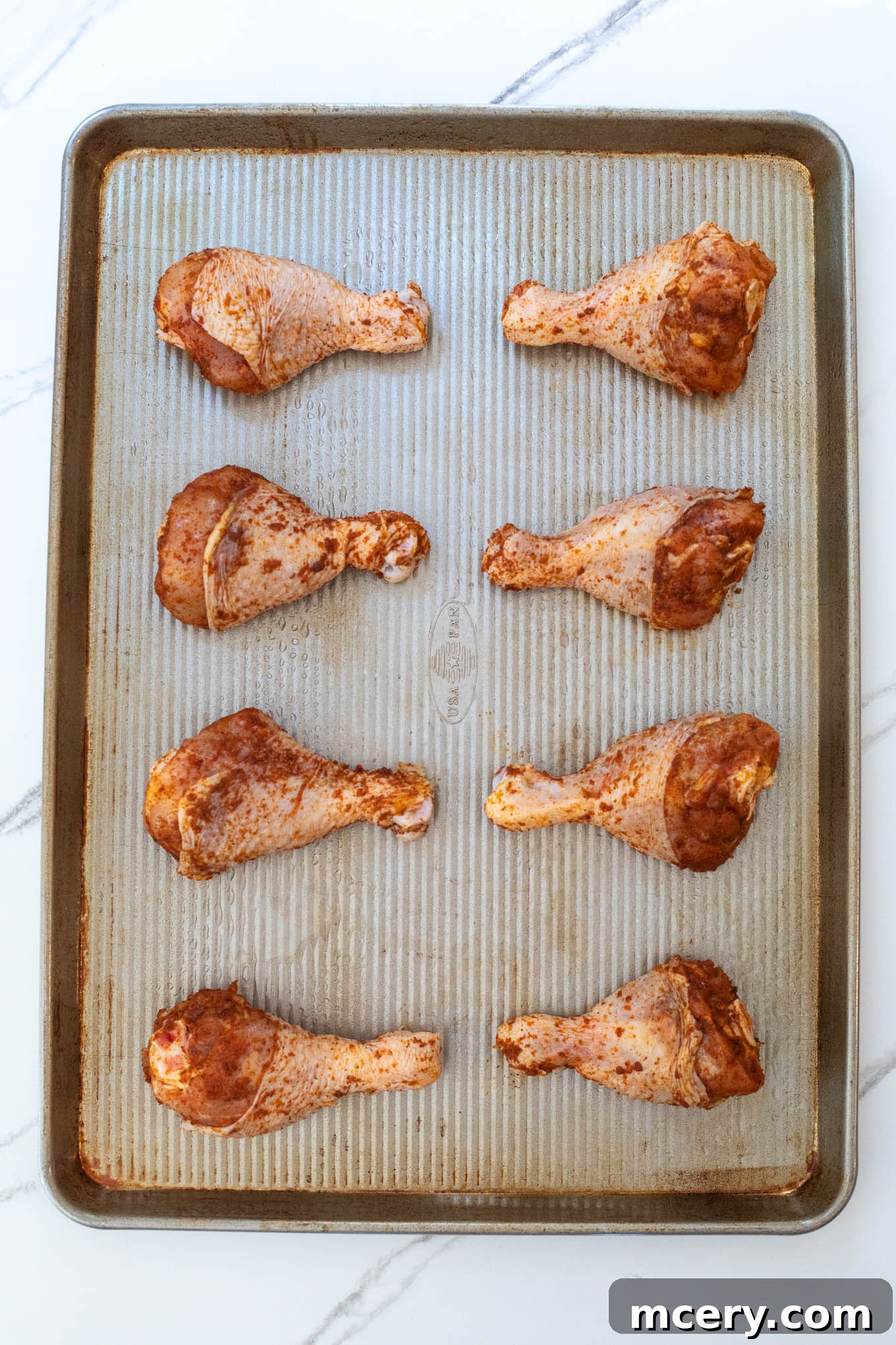 Sweet & Smoky Oven-Baked BBQ Drumsticks 7 Seasoned chicken drumsticks arranged in a single layer on a parchment-lined sheet pan.