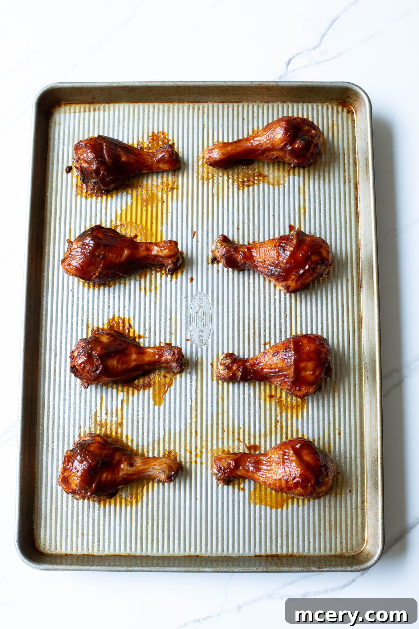 Sweet & Smoky Oven-Baked BBQ Drumsticks 9 Roasted BBQ chicken legs on a sheet pan, looking golden and caramelized.