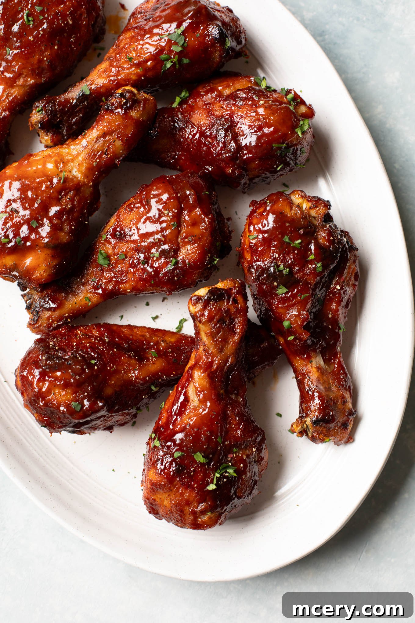 Sweet & Smoky Oven-Baked BBQ Drumsticks 10 Close up of perfectly roasted bbq chicken legs arranged on a white platter, garnished with fresh herbs.