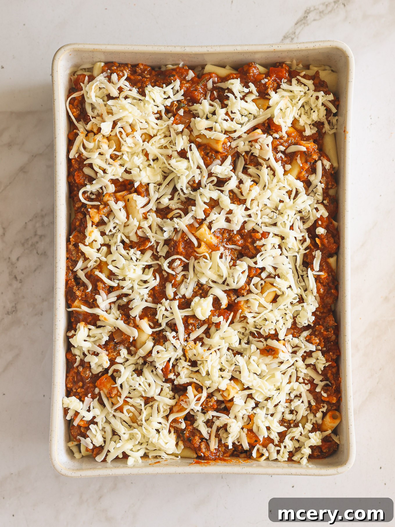 Golden Baked Ziti Delight 11 A fully layered baked ziti pasta dish, topped with mozzarella cheese, ready for baking.