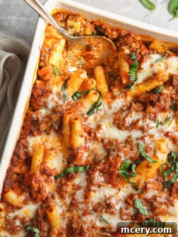 A large serving of baked ziti with meat and cheese, scooped into a white baking dish with a spoon.