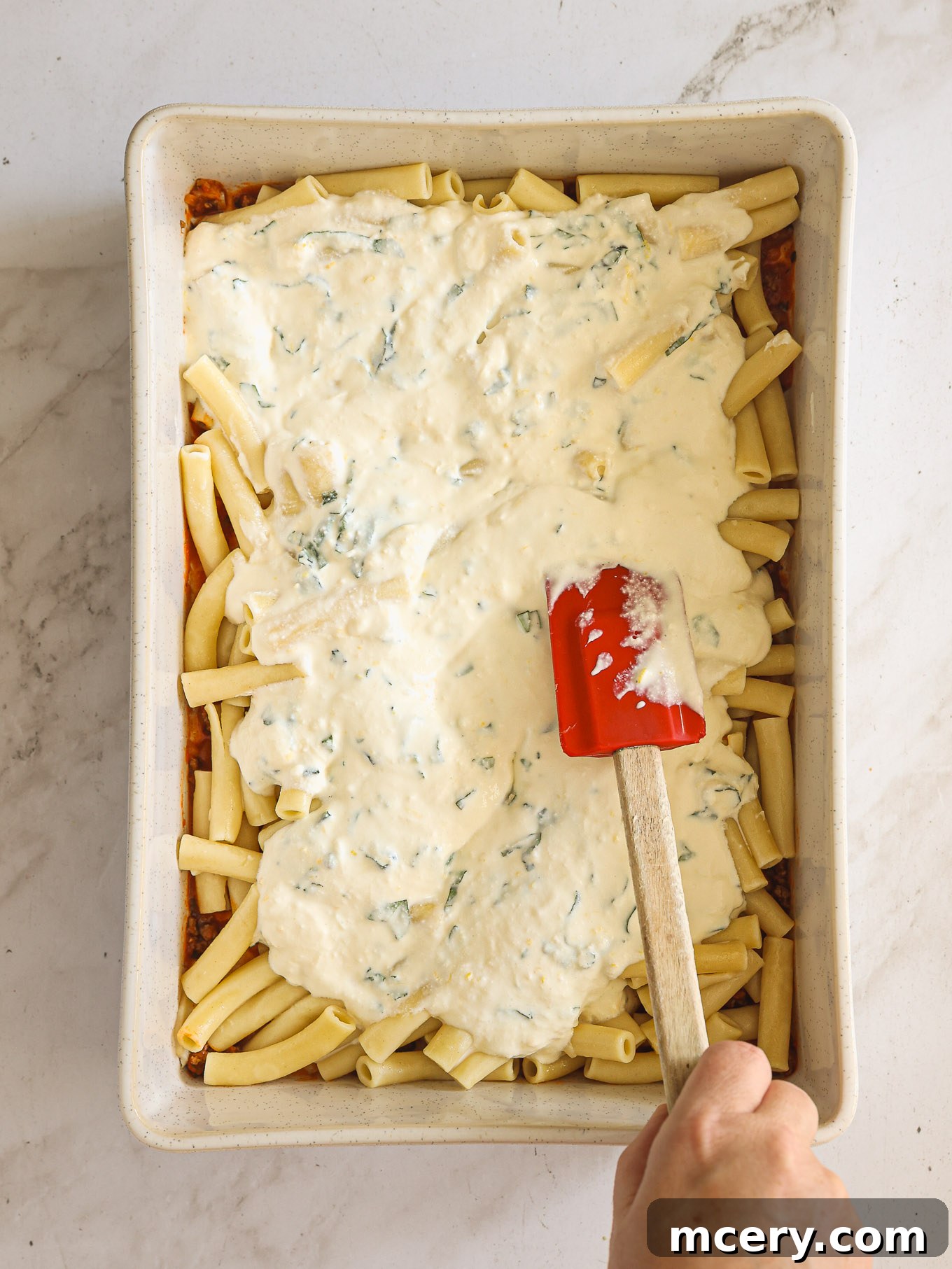 Golden Baked Ziti Delight 9 Creamy ricotta cheese mixture spread over cooked ziti pasta in a baking dish.