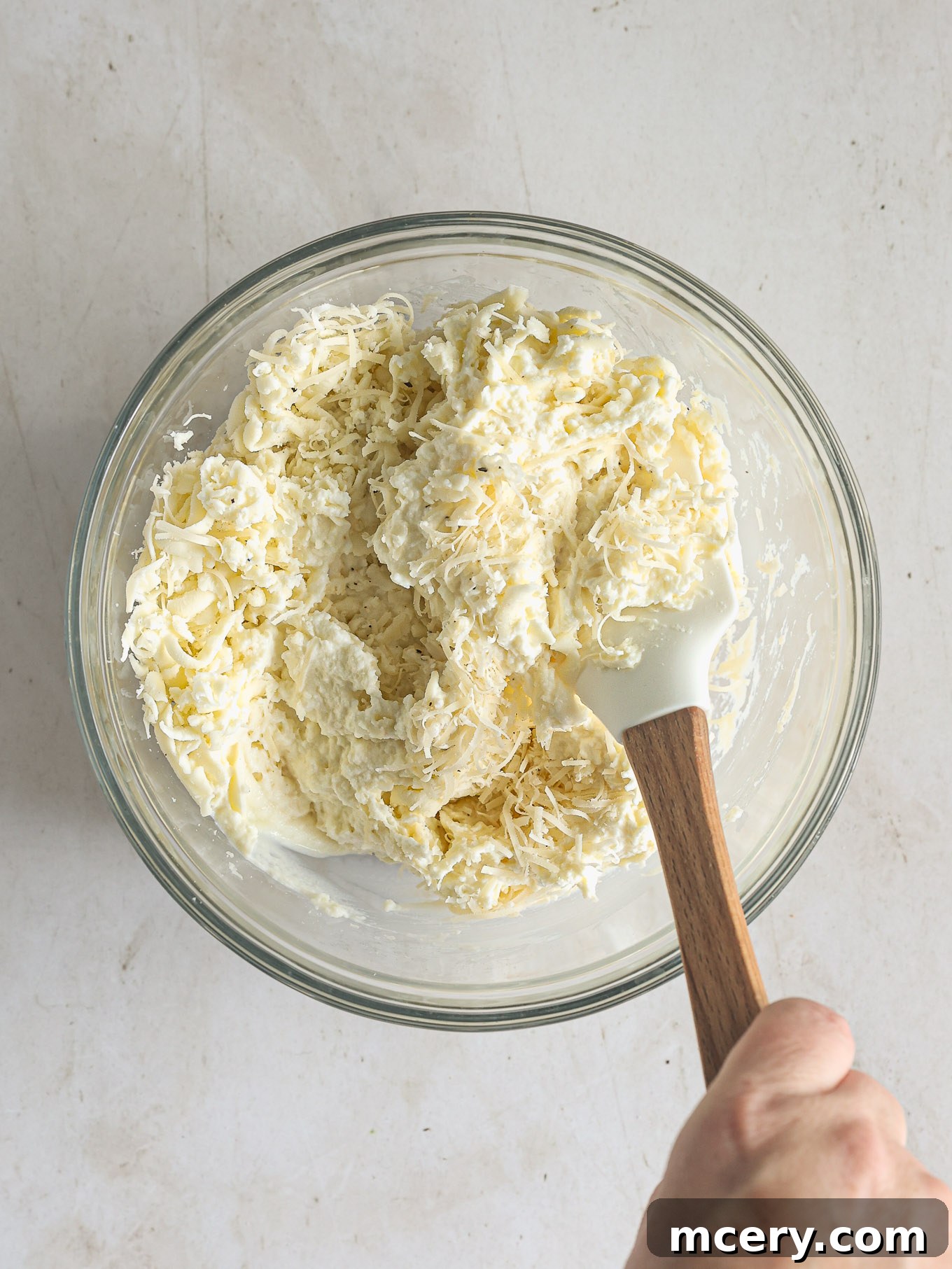 Effortless Creamy Ricotta Spaghetti Bake 7 A creamy mixture of ricotta cheese, shredded mozzarella, and grated Parmesan cheese in a mixing bowl, seasoned and ready for layering.