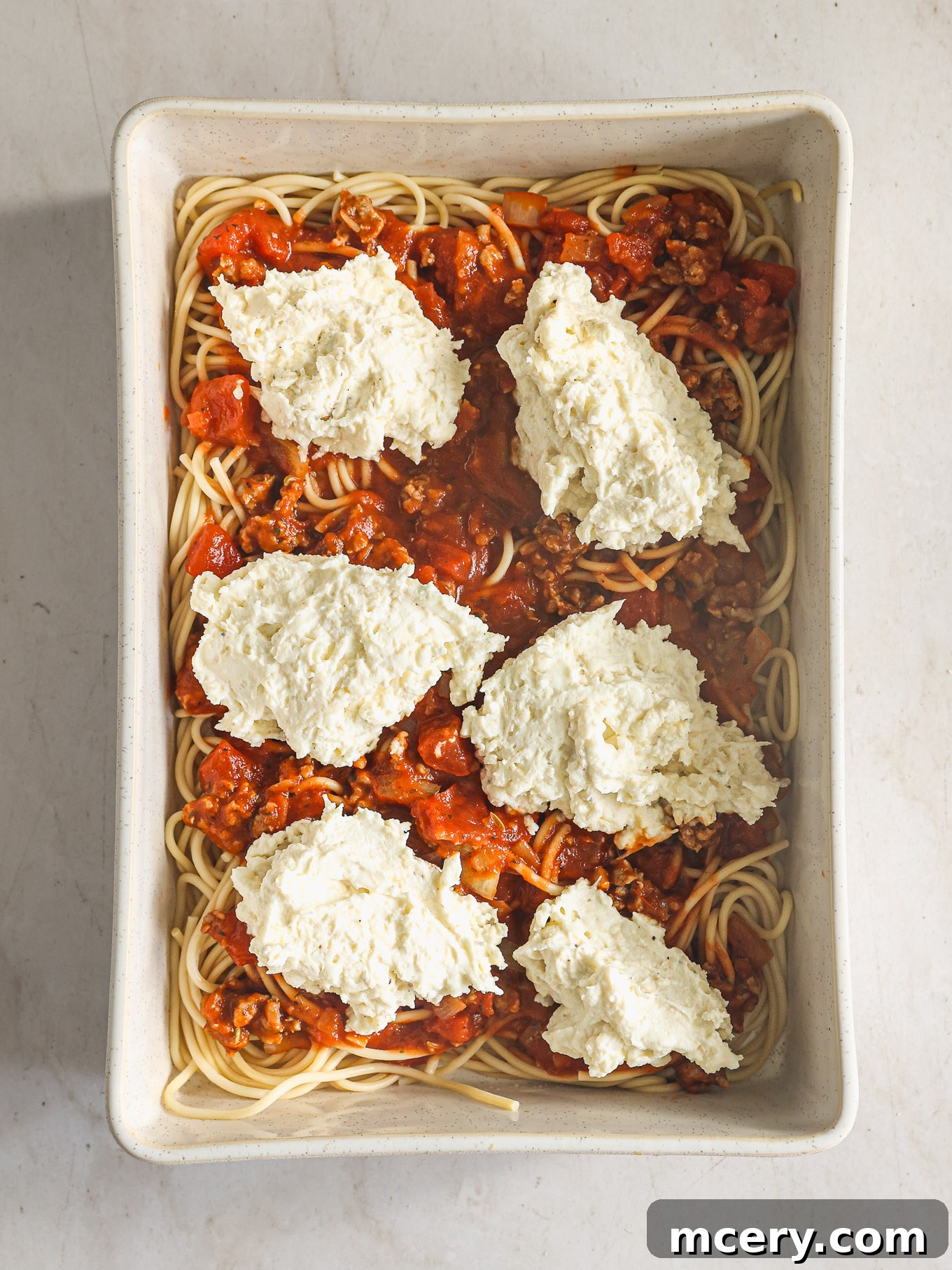 Effortless Creamy Ricotta Spaghetti Bake 8 The first layer of cooked spaghetti spread in a greased baking dish, topped with half of the rich meat sauce and dollops of the creamy ricotta cheese mixture.