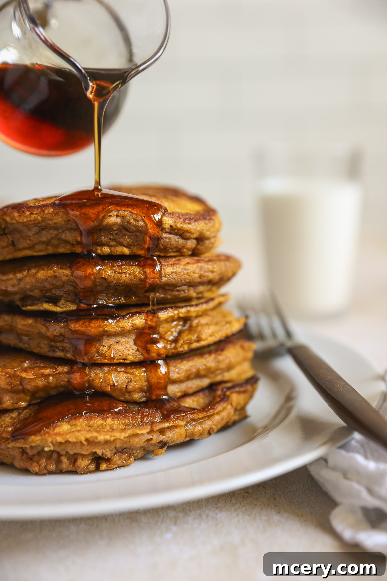 Whip Up Fluffy Pumpkin Pancakes 2 Stacked pumpkin pancakes drizzled with maple syrup, garnished with a sprinkle of cinnamon and a few cranberries, set on a rustic wooden board.