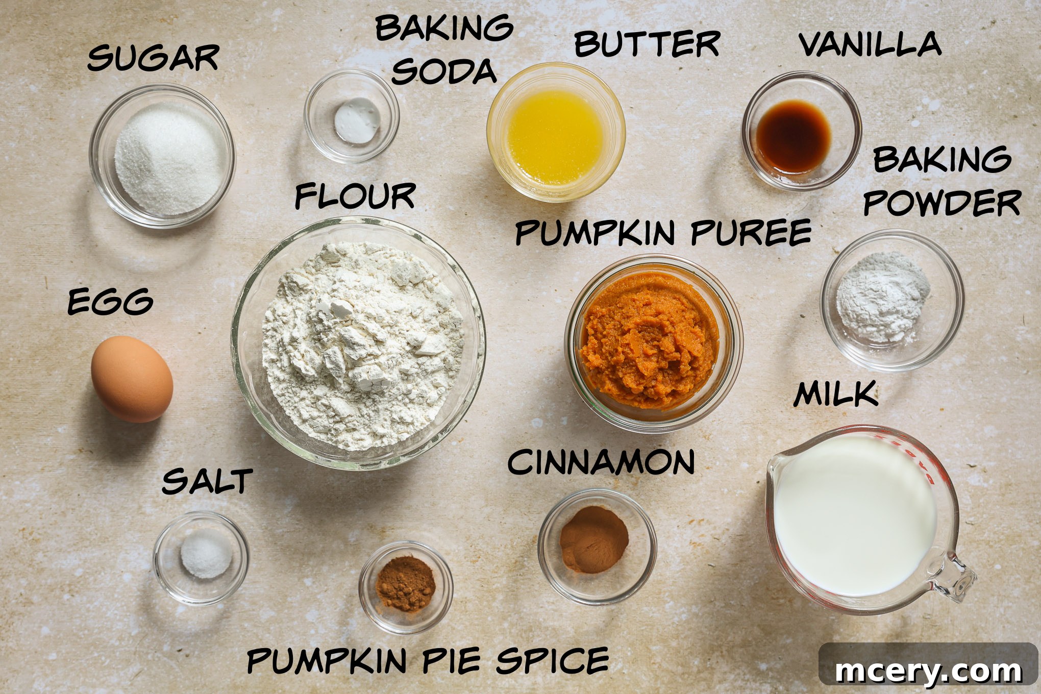 Whip Up Fluffy Pumpkin Pancakes 3 A collection of fresh ingredients laid out on a wooden surface, including a can of pumpkin puree, milk, eggs, flour, sugar, and various spices.