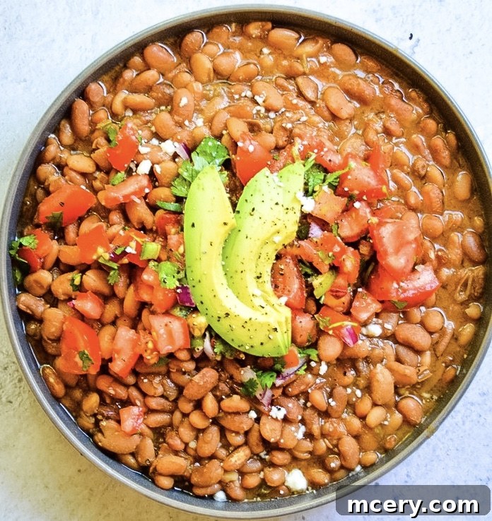 Speedy & Savory Instant Pot Pinto Beans 4 A flat lay of fresh ingredients including dry pinto beans, a whole onion, garlic cloves, a jalapeño, a tomato, and various spices, arranged on a rustic wooden surface.