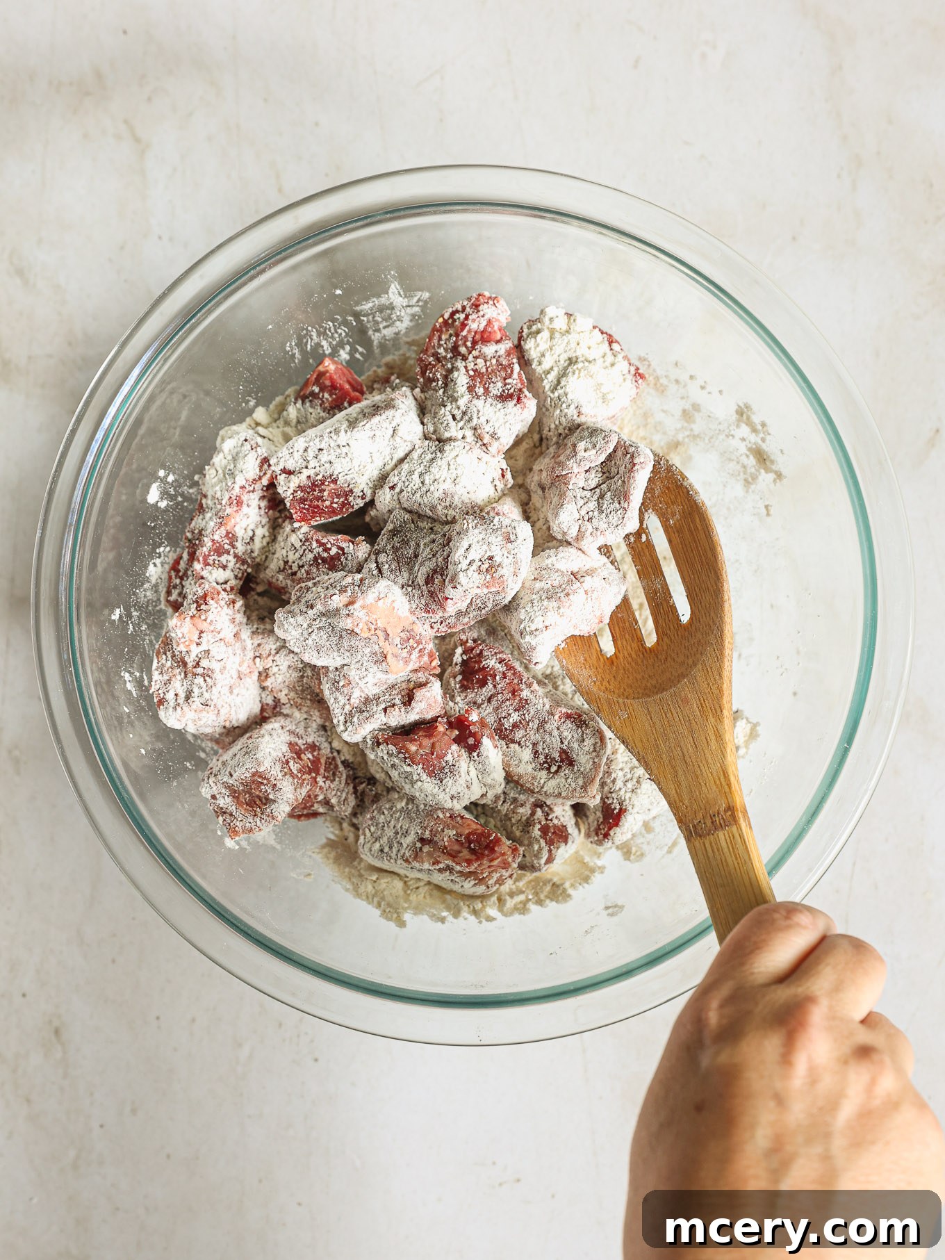 Beef cubes generously seasoned with salt, pepper, and lightly dusted with flour, meticulously prepared in a clear glass bowl.