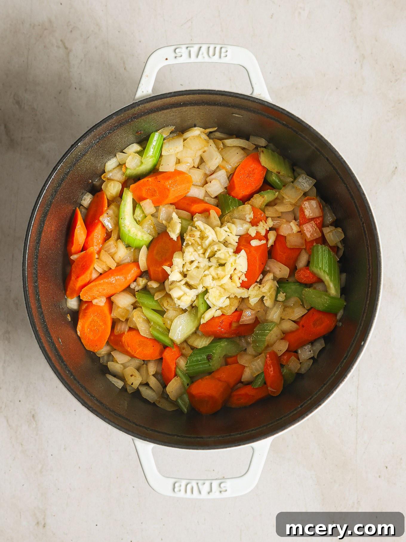 Fragrant sautéed onions, carrots, and celery gently cooking in the Dutch oven, forming the aromatic base of the stew.