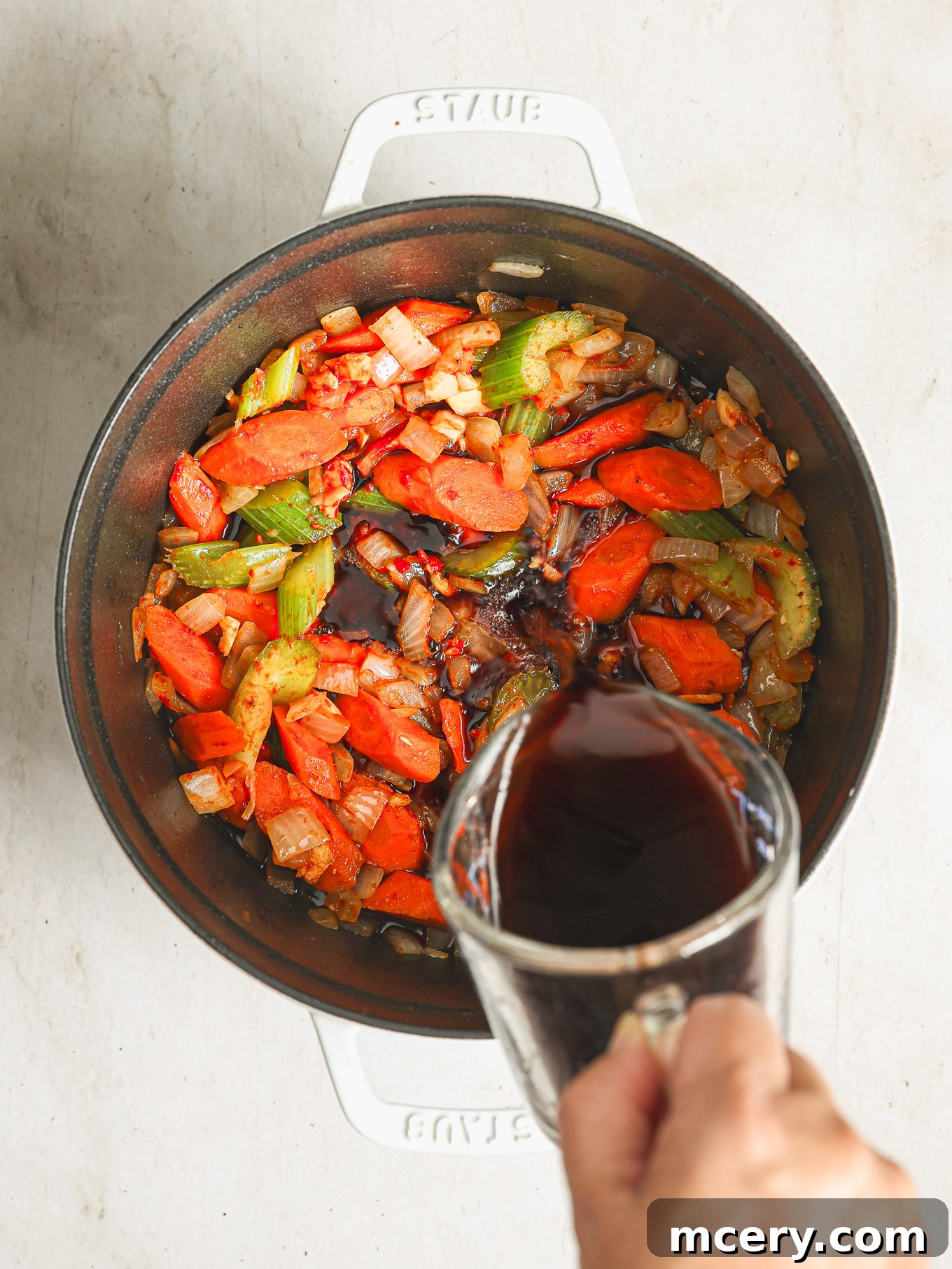 The process of deglazing: red wine poured into the hot Dutch oven, actively scraping up all the browned bits.