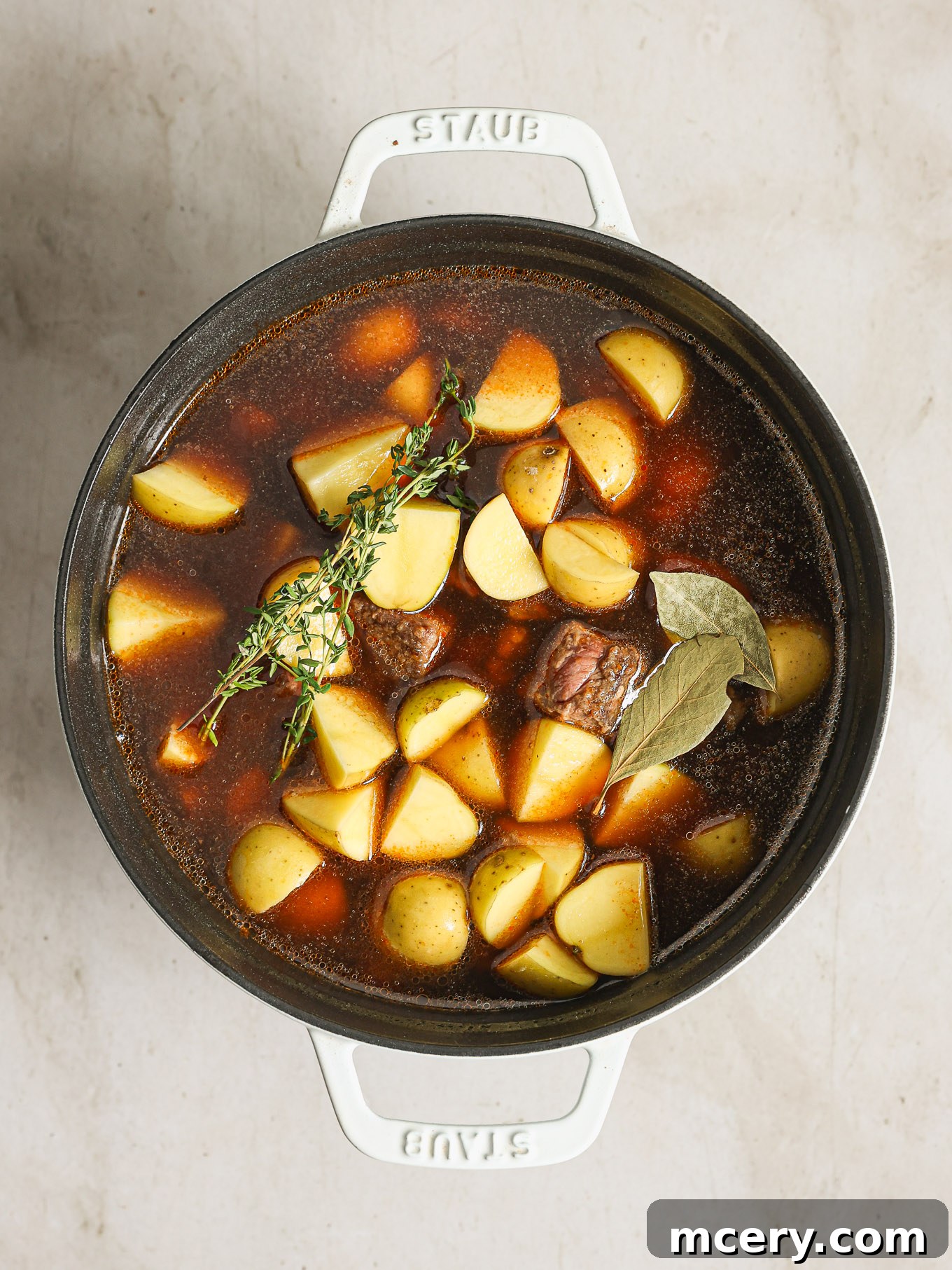 All the core ingredients, including browned beef and tender potatoes, combined and simmering harmoniously in a Dutch oven.
