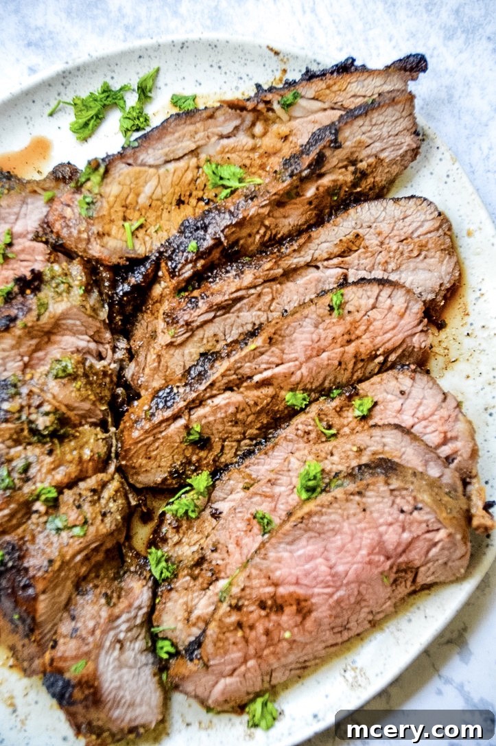 Close-up of a Tri-Tip roast searing in a hot cast iron skillet on a stovetop, developing a caramelized crust.