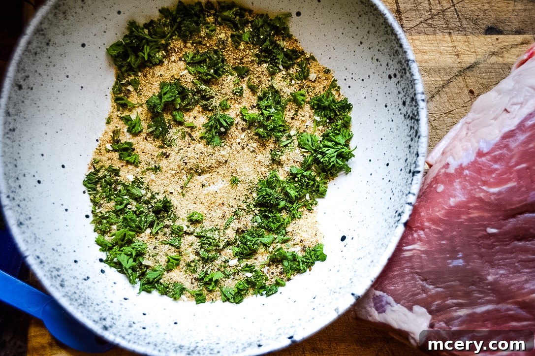 A hand meticulously rubbing a flavorful blend of spices over a raw Tri-Tip roast, ensuring full coverage.