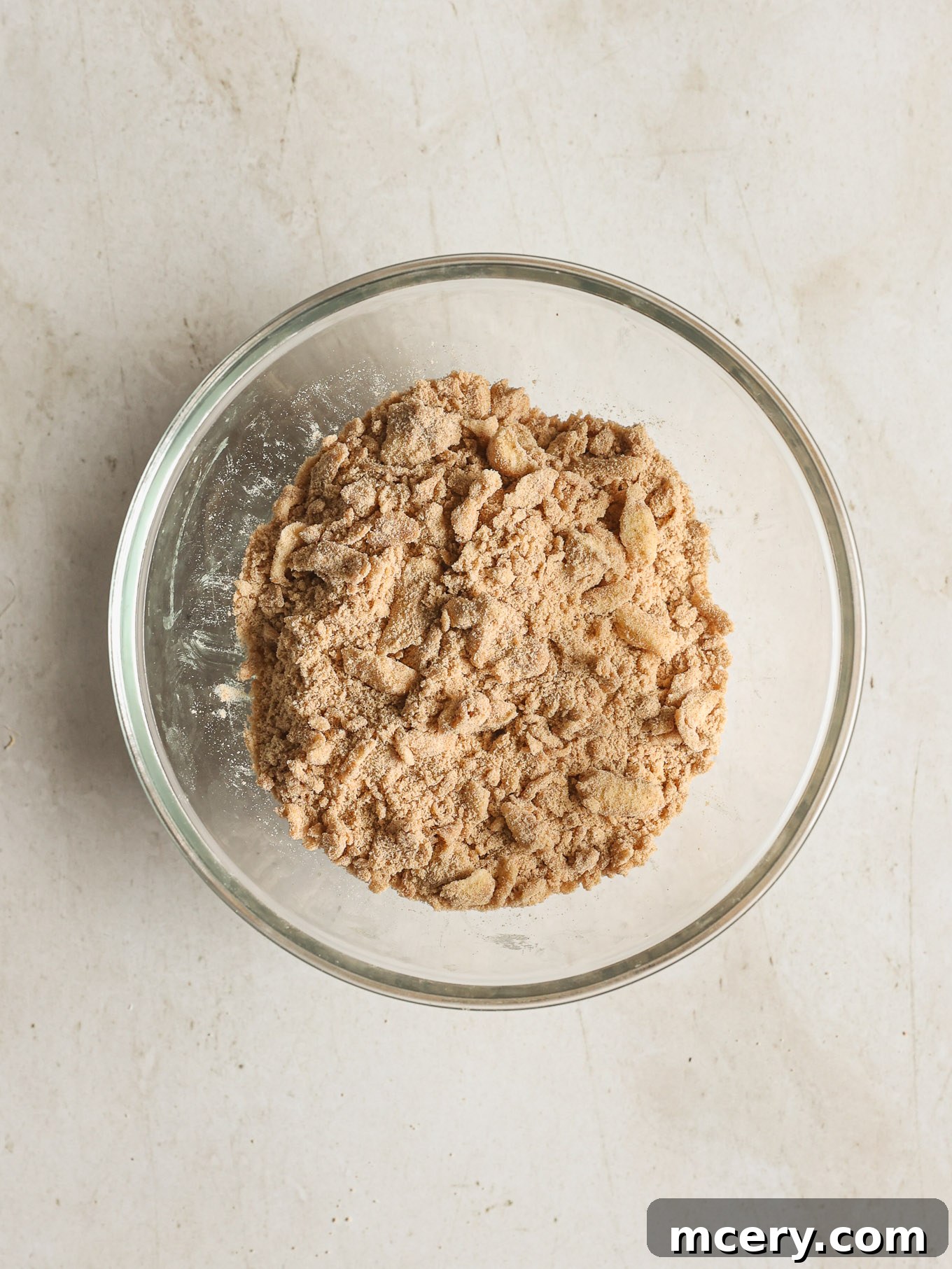 Cozy Pumpkin Crumble Coffee Cake 5 Cubed cold unsalted butter is being cut into the dry streusel mixture in a glass bowl using a pastry cutter, creating a crumbly texture.