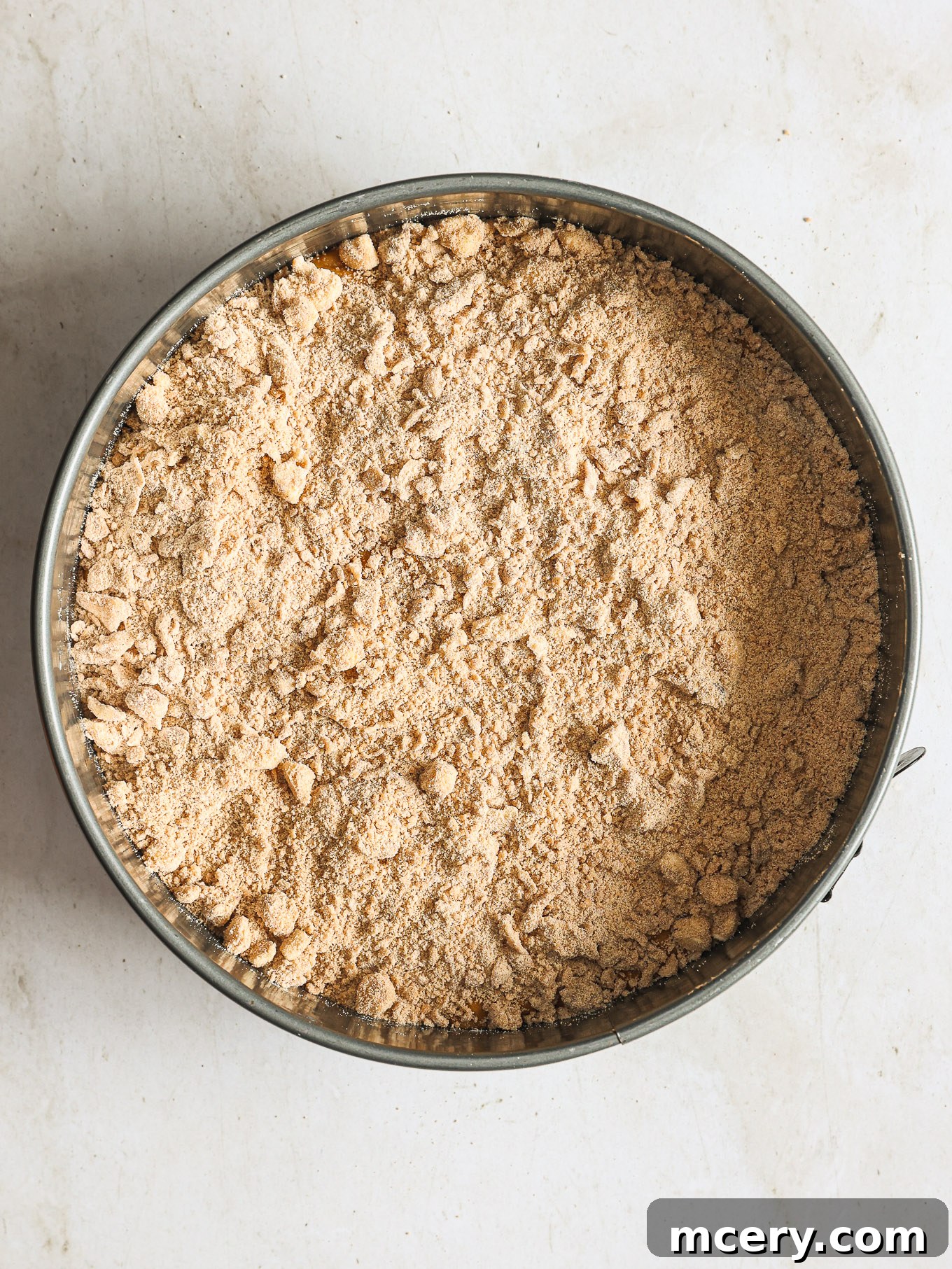 Cozy Pumpkin Crumble Coffee Cake 9 Pumpkin coffee cake batter evenly spread in a springform pan and generously topped with a layer of streusel, ready for baking.