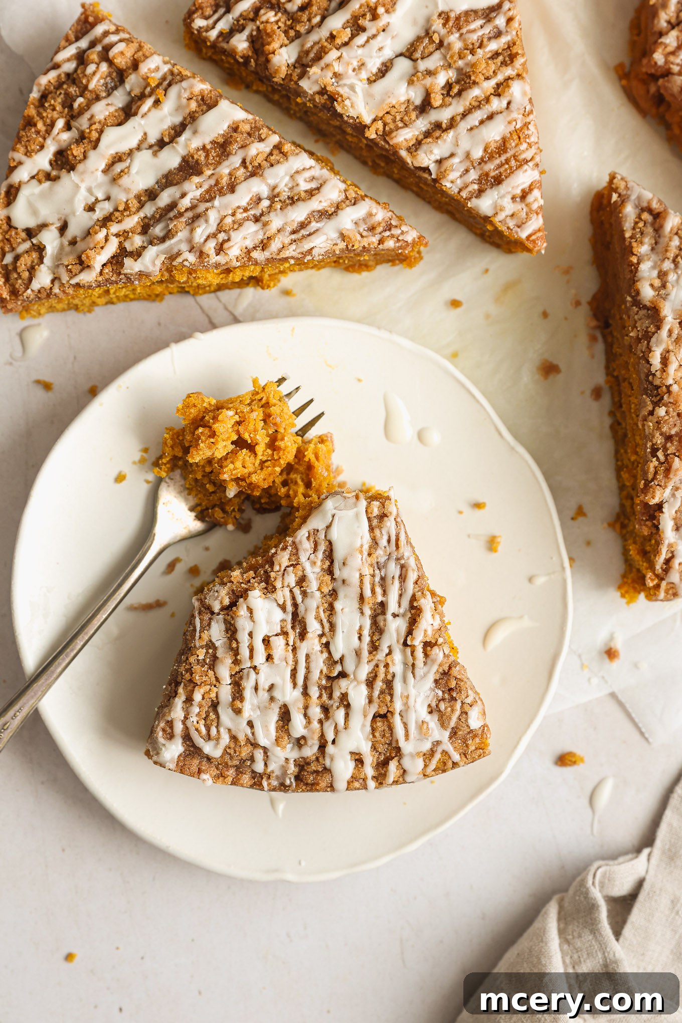 Cozy Pumpkin Crumble Coffee Cake 10 A close-up view of beautifully sliced coffee cake, showcasing its moist pumpkin interior, rich streusel topping, and a delicate drizzle of glaze, presented on a white surface.