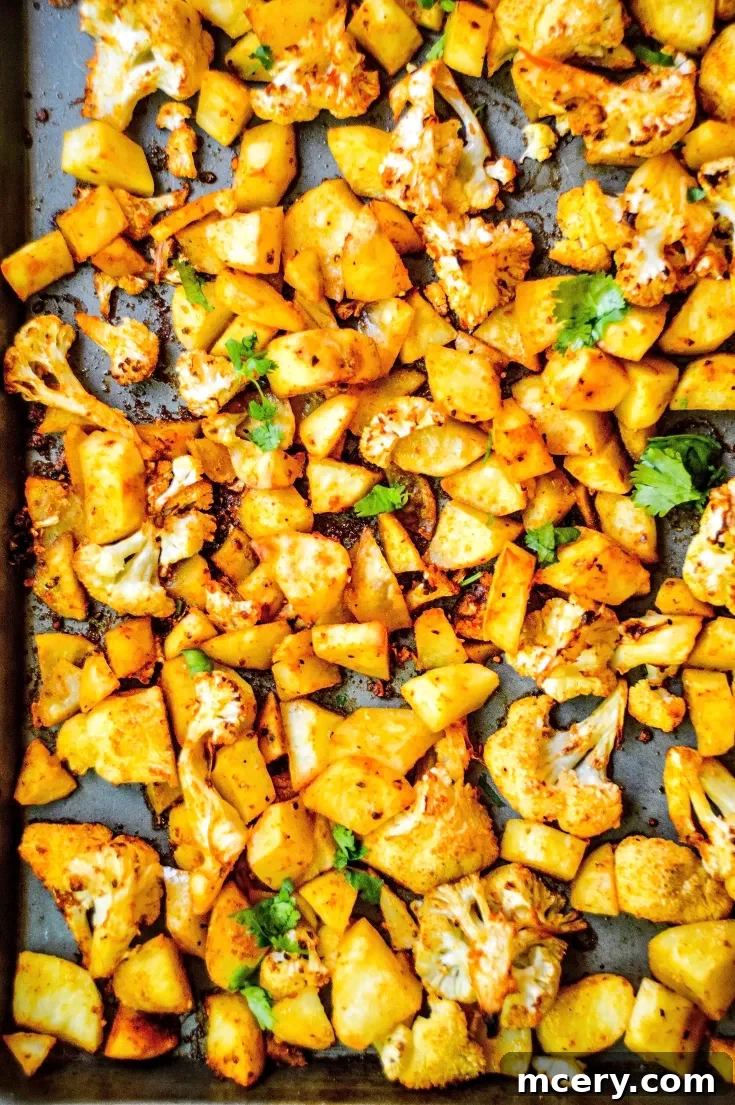 A baking sheet filled with roasted cauliflower and diced potatoes, seasoned with spices and garnished with fresh herbs. The vegetables are golden brown, suggesting they are crispy and well-cooked.