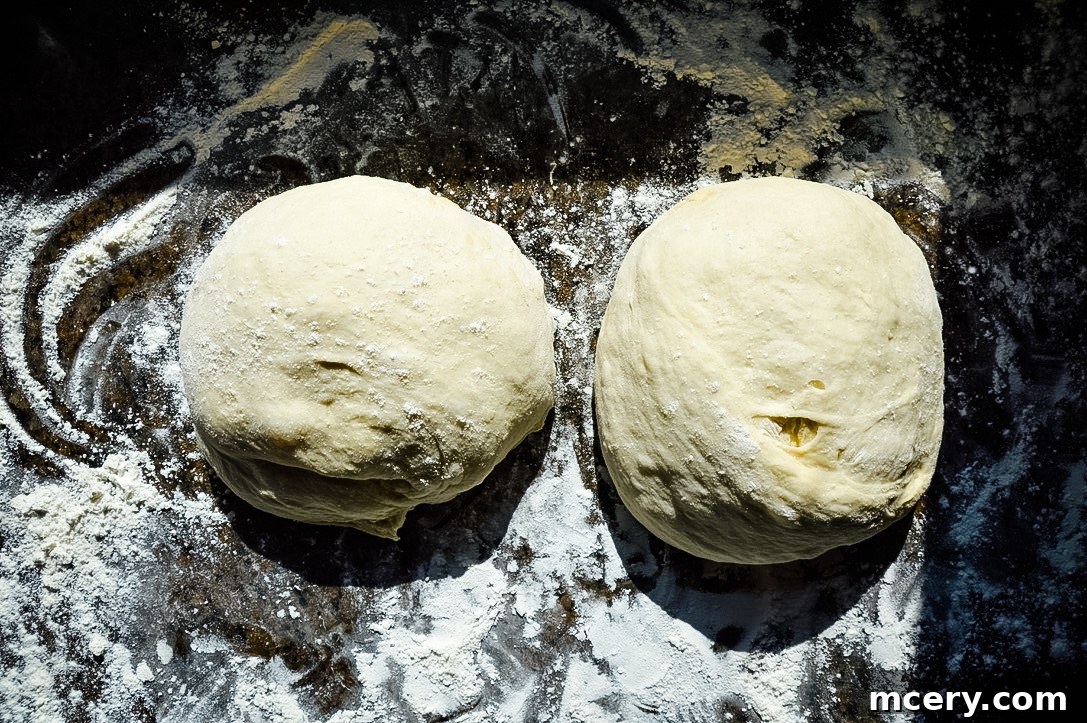 Fast and Easy Food Processor Pizza Dough 6 A portion of pizza dough being rolled out into a circular shape on a floured wooden surface, with a rolling pin beside it.