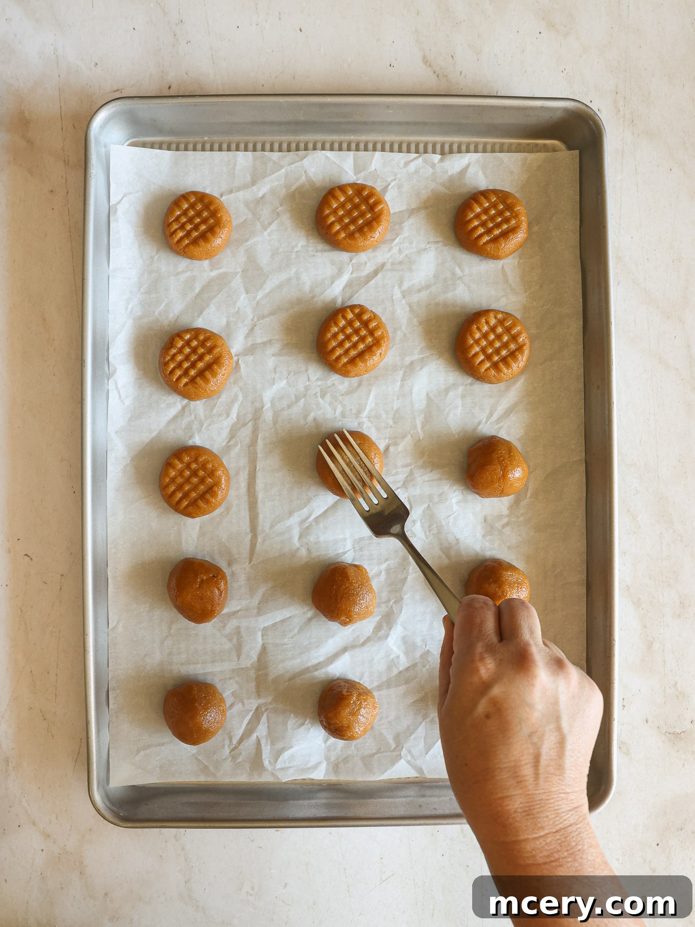 Effortless 4-Ingredient Peanut Butter Cookies 7 Peanut butter cookie dough balls gently flattened with a fork, creating the traditional crisscross pattern.