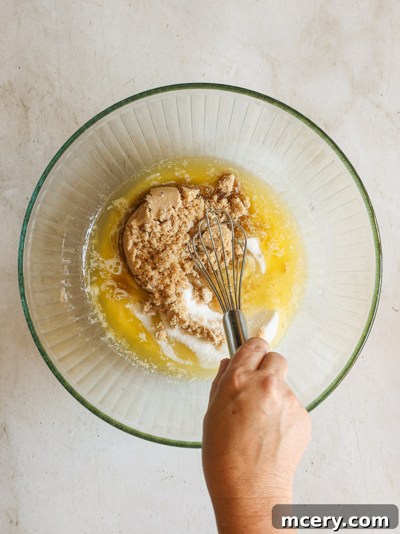No-Bake Crispy Cornflake Treats 5 Wet ingredients for cornflake cookies, including melted butter, brown sugar, and cane sugar, whisked in a glass bowl.