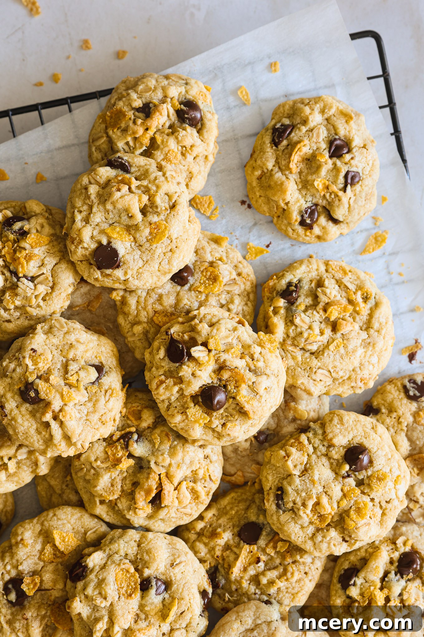 No-Bake Crispy Cornflake Treats 10 A stack of golden-brown baked cornflake cookies cooling on a wire rack, with some chocolate chips visible.