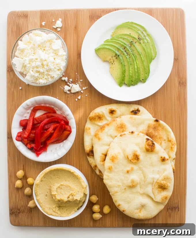 Easy Hummus Naan Toasts: 3 Delicious Variations 2 Close-up of a mini naan toast with hummus, roasted red pepper, avocado slices, and crumbled feta cheese.