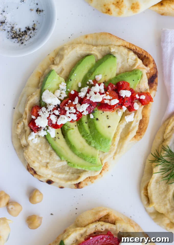 Easy Hummus Naan Toasts: 3 Delicious Variations 3 Overhead view of various fresh ingredients laid out, including sliced avocado, roasted red peppers, feta, cucumber, tzatziki, tomatoes, mozzarella, and basil, ready for naan toast toppings.