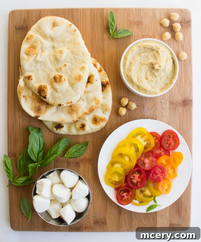 Easy Hummus Naan Toasts: 3 Delicious Variations 6 A gourmet mini naan toast topped with hummus, slices of ripe tomato, small mozzarella balls, and fresh basil leaves, with a drizzle of olive oil.