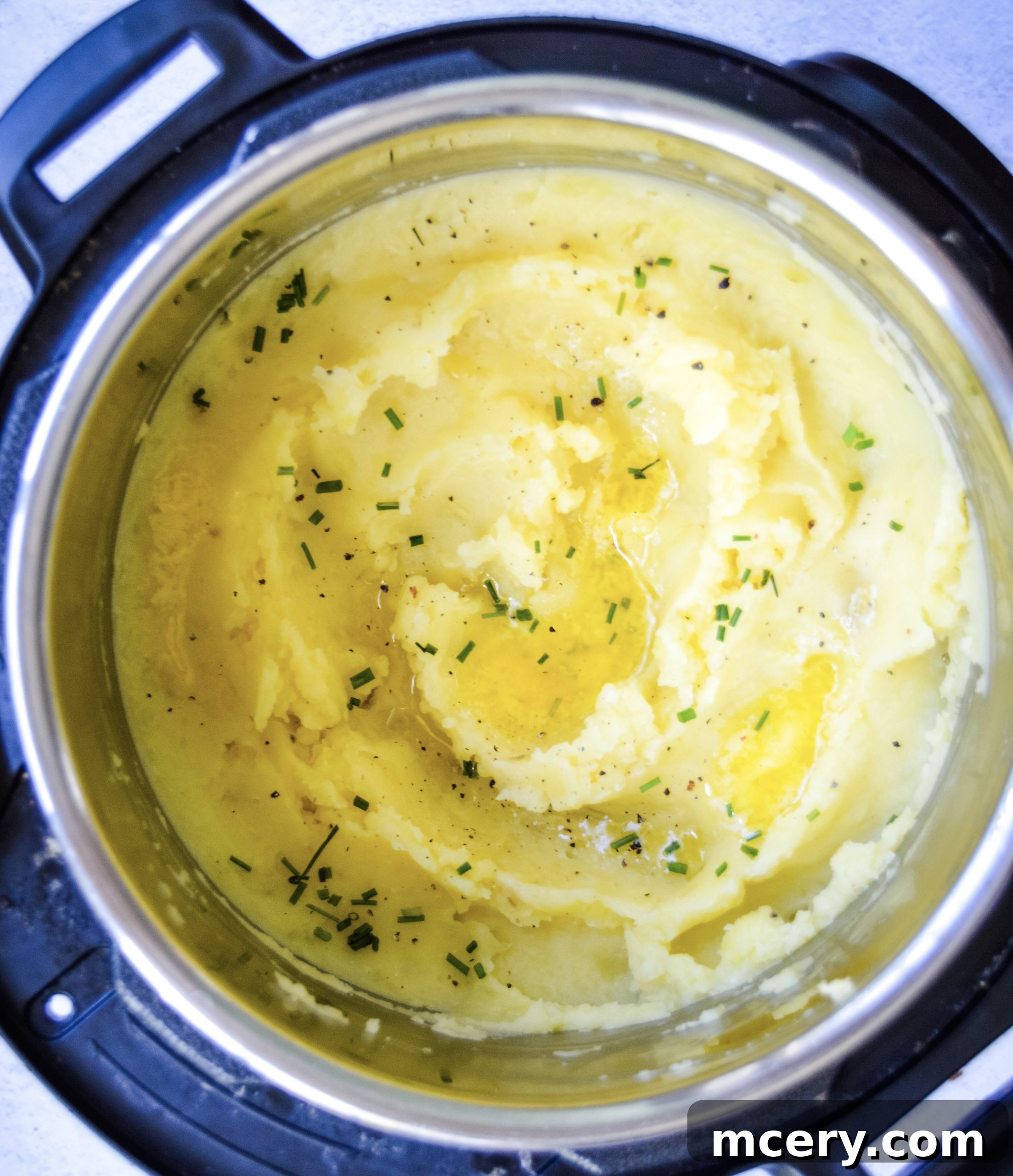 A top-down view of a bowl of fluffy Instant Pot Garlic Mashed Potatoes garnished with fresh chives and a pat of melting butter.