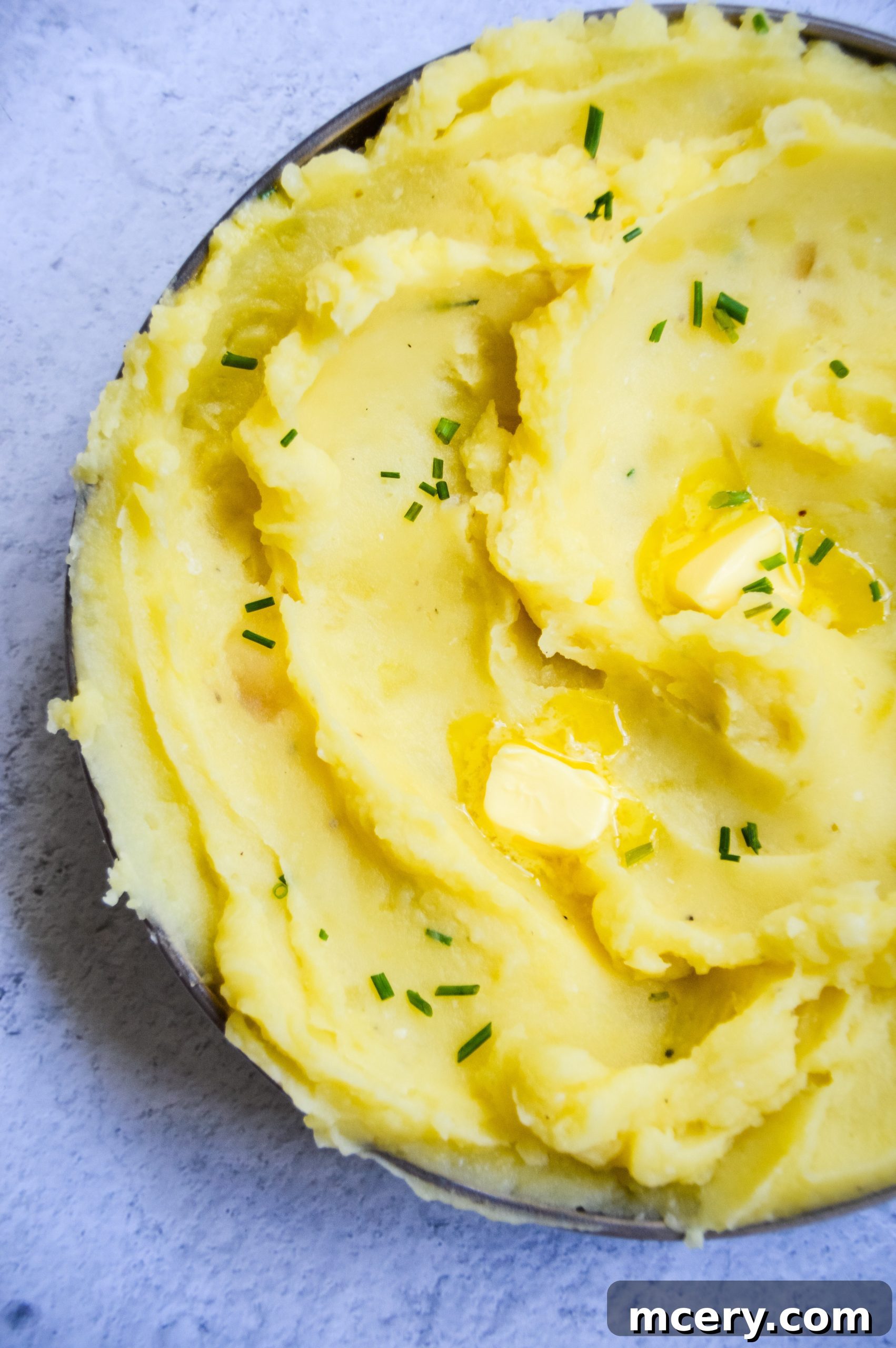 A close-up shot of fluffy Instant Pot garlic mashed potatoes, ready to be served, topped with a dollop of butter and fresh chives.