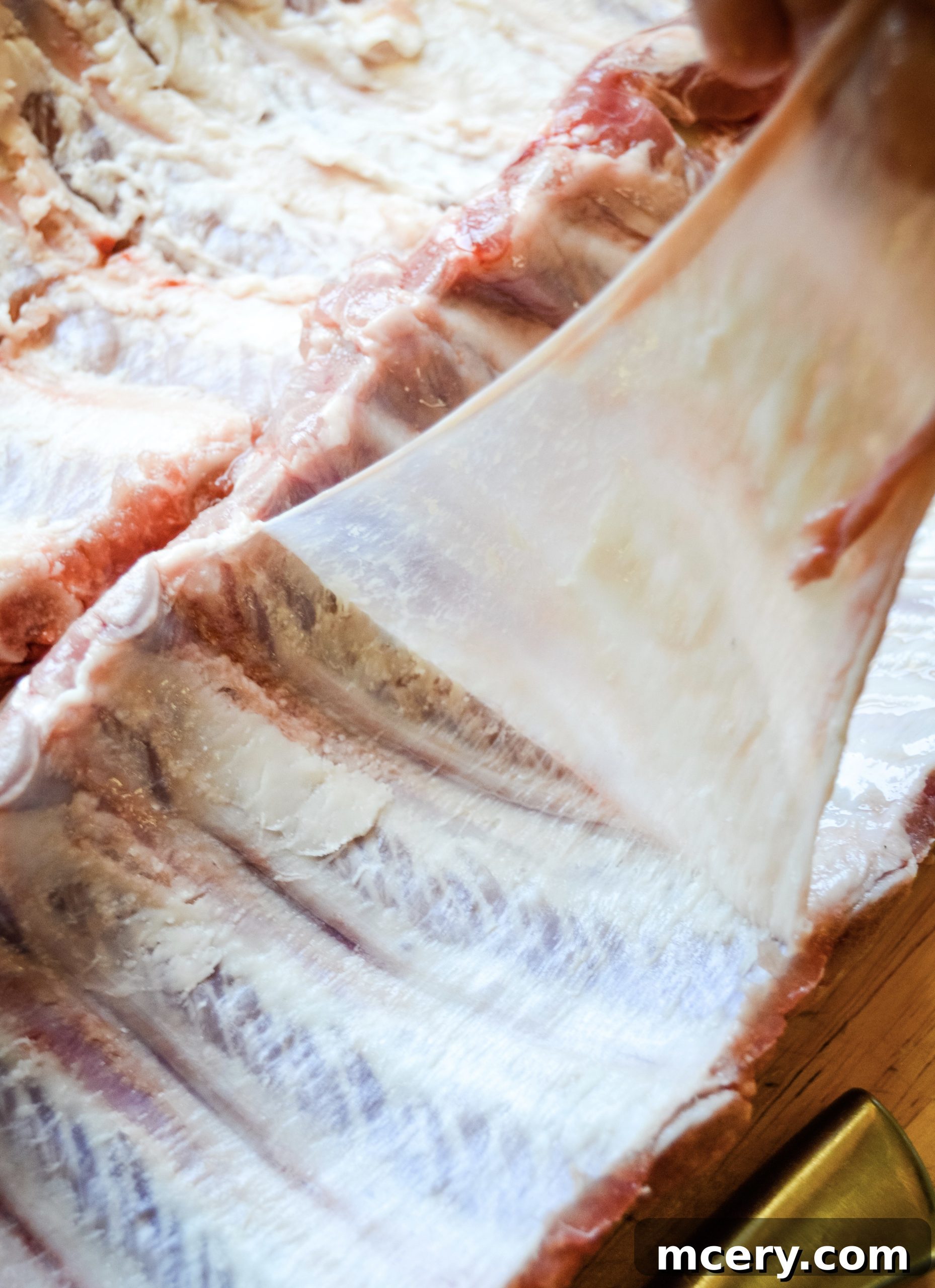 Paleo Rubbed Gas Grilled Pork Ribs 5 Hands pulling the silver skin membrane off the back of a rack of pork ribs.