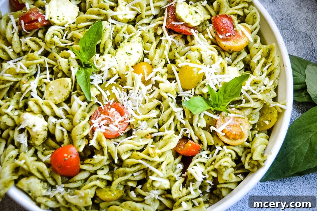 Delicious Spinach Pesto Pasta Salad A bright, colorful Spinach Pesto Pasta Salad in a white bowl, garnished with fresh basil and cherry tomatoes.